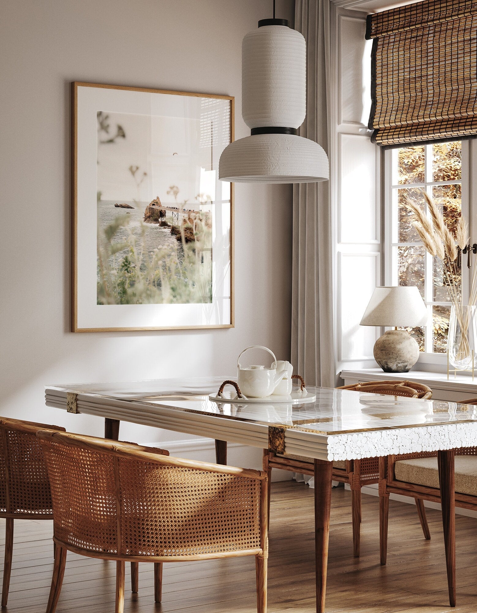 A cozy dining room with a Roche de le Vierge table, wicker chairs, pendant lamp, bamboo blinds, and nature artwork.
