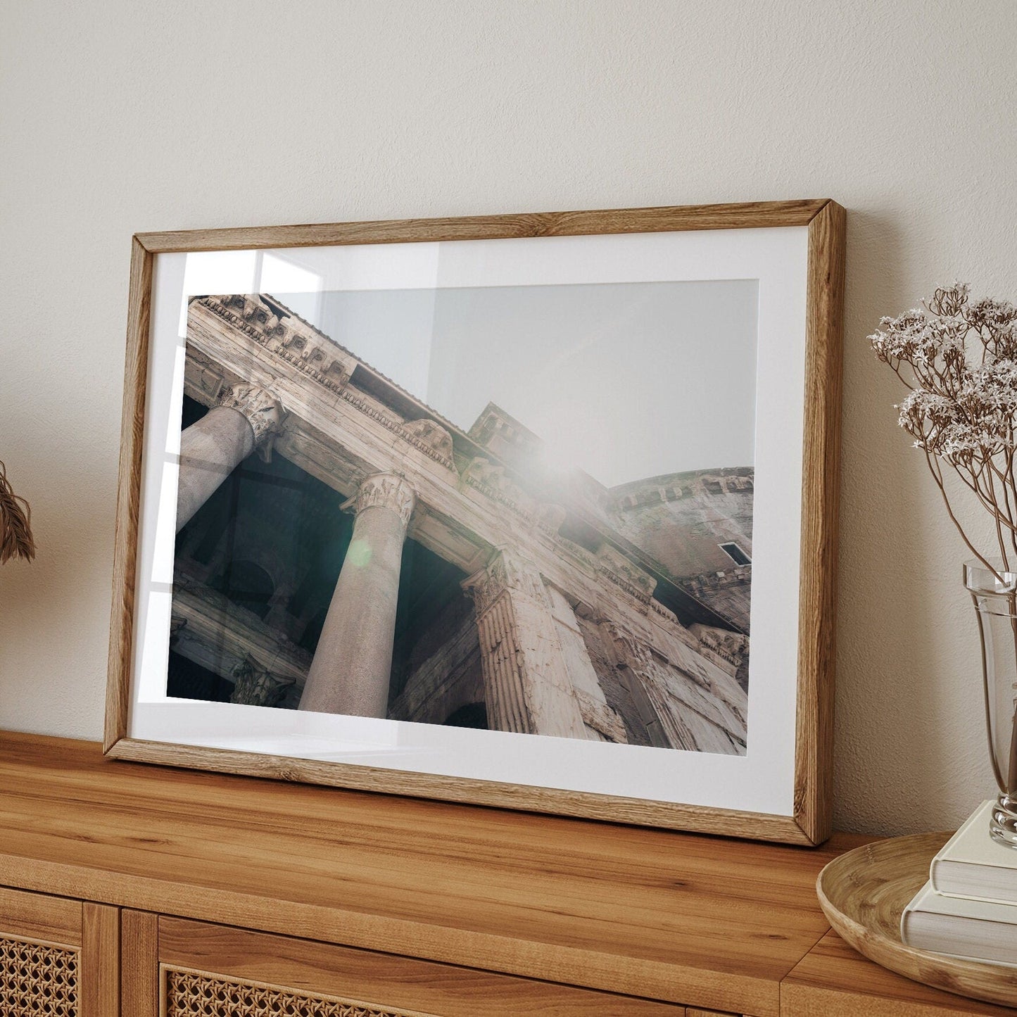 Roman Pantheon I: A framed photo of ancient ruins with sunlight on a wooden cabinet, adorned with dried flowers.