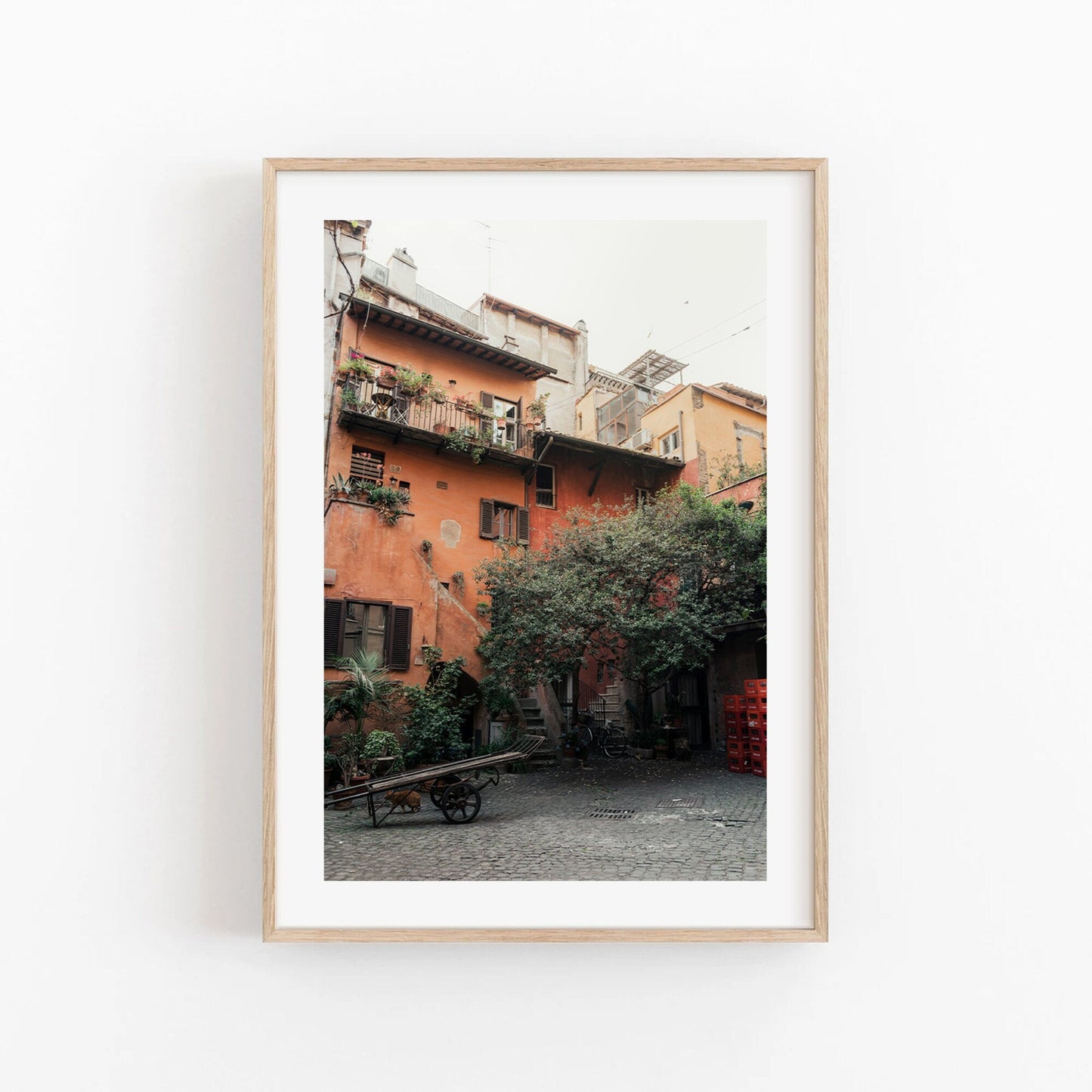 Framed photo of a quaint courtyard with rustic orange building, balconies, and greenery. (Product: Rome Courtyard).