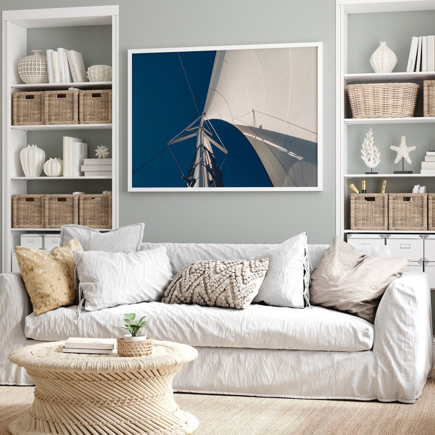 A cozy living room with a white sofa, wicker table, Sailing Bliss photo on the wall, and shelves holding baskets and decor.