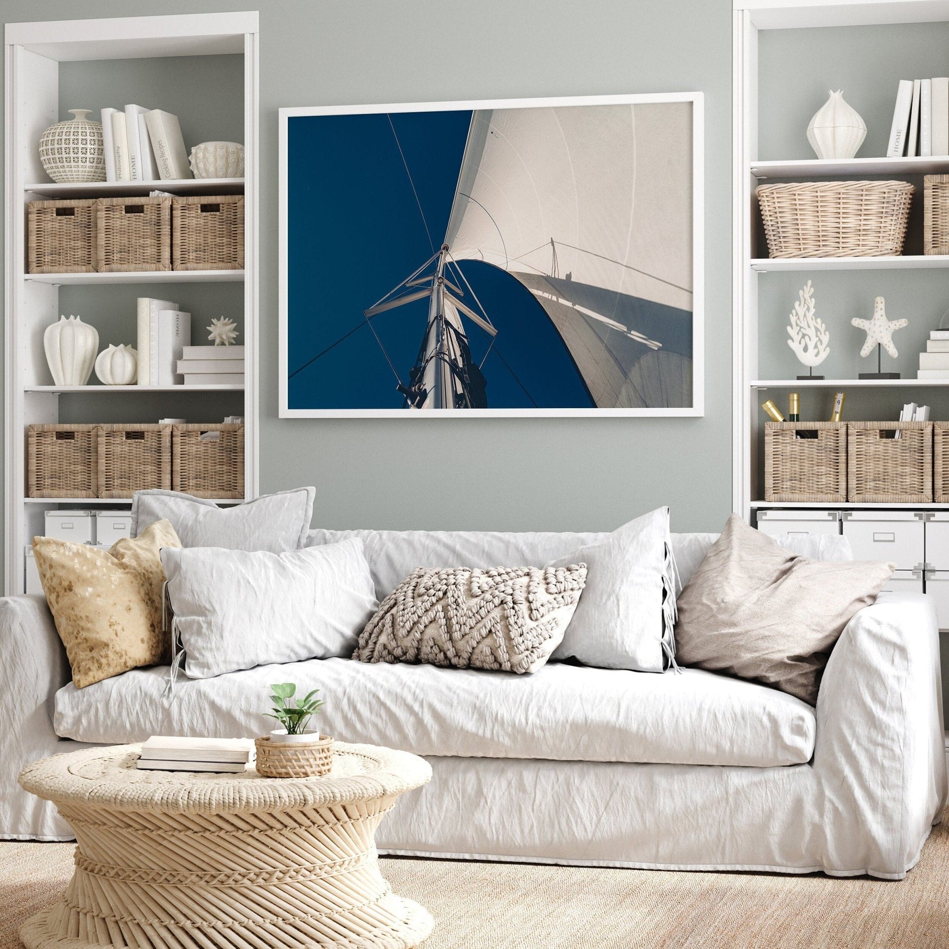 A cozy living room with a white sofa, wicker table, Sailing Bliss photo on the wall, and shelves holding baskets and decor.