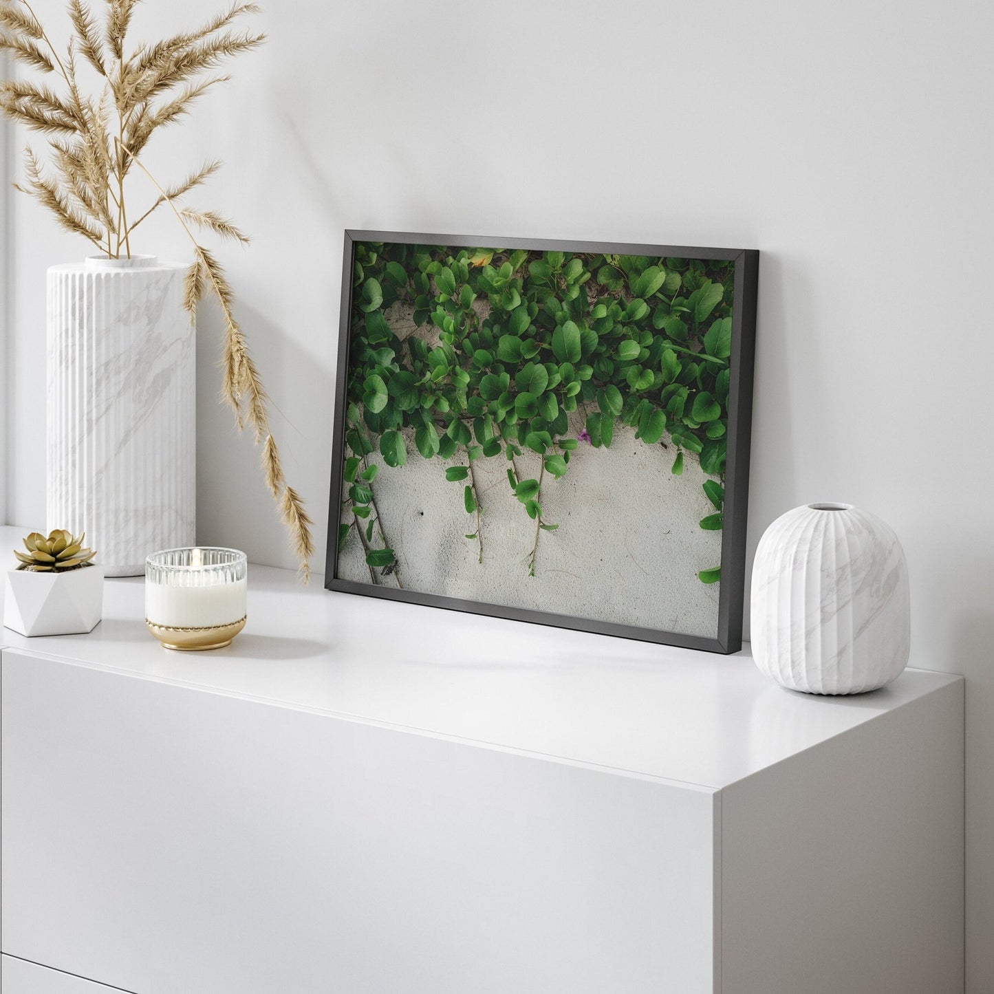 Sandy Garden I framed picture of green leaves on a white shelf with vases and candles nearby.