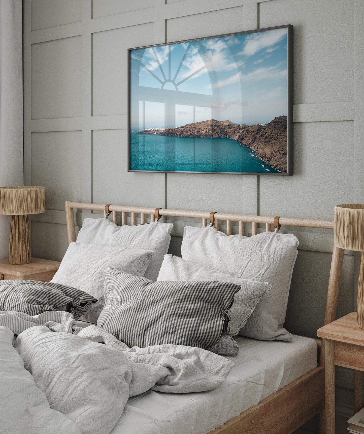 Cozy bedroom with a wooden bed, white bedding, and Santorini Mountain photo on the wall, softly lit by natural light.