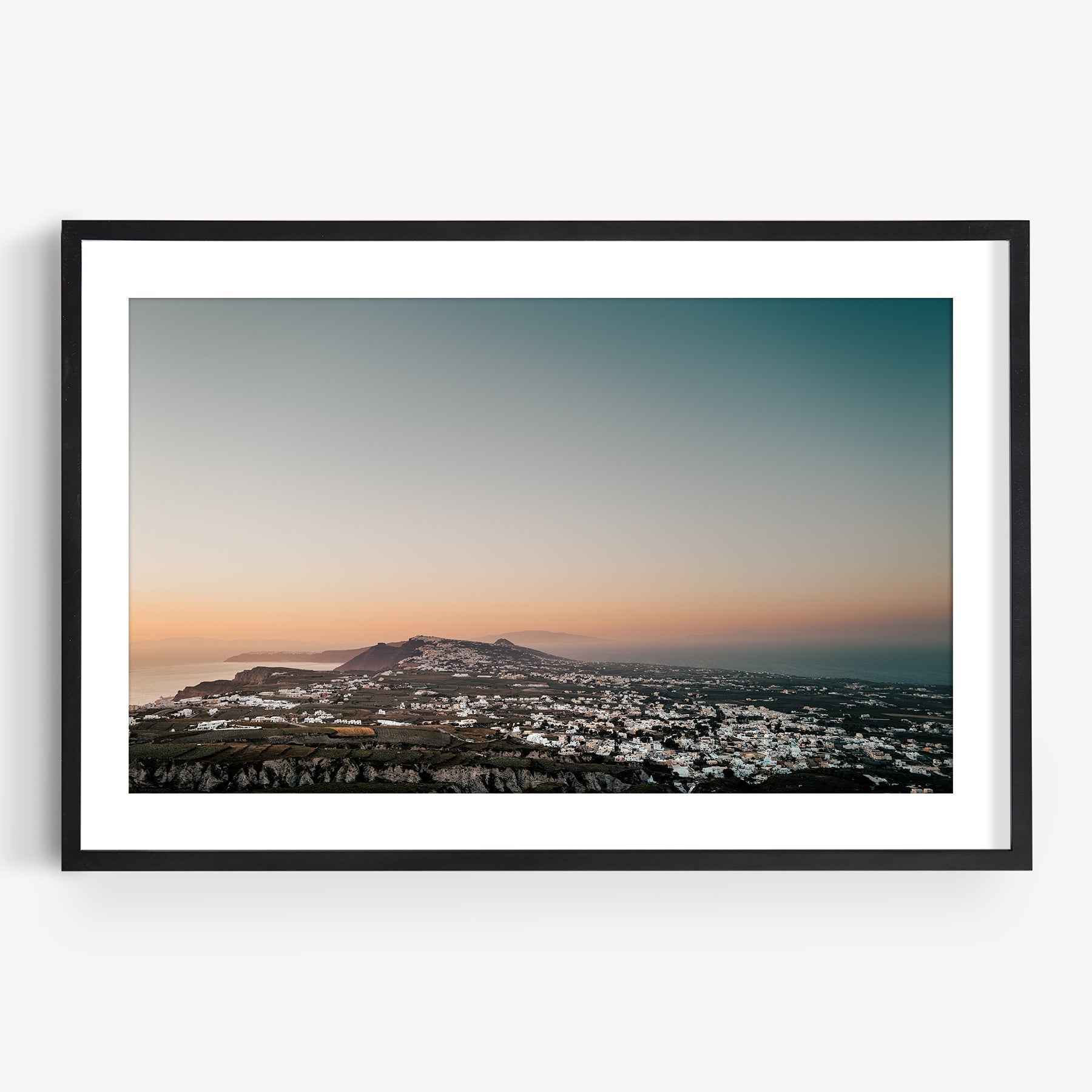 Santorinis Glow: A framed photo of a coastal town at sunset with white buildings and a hilly landscape.