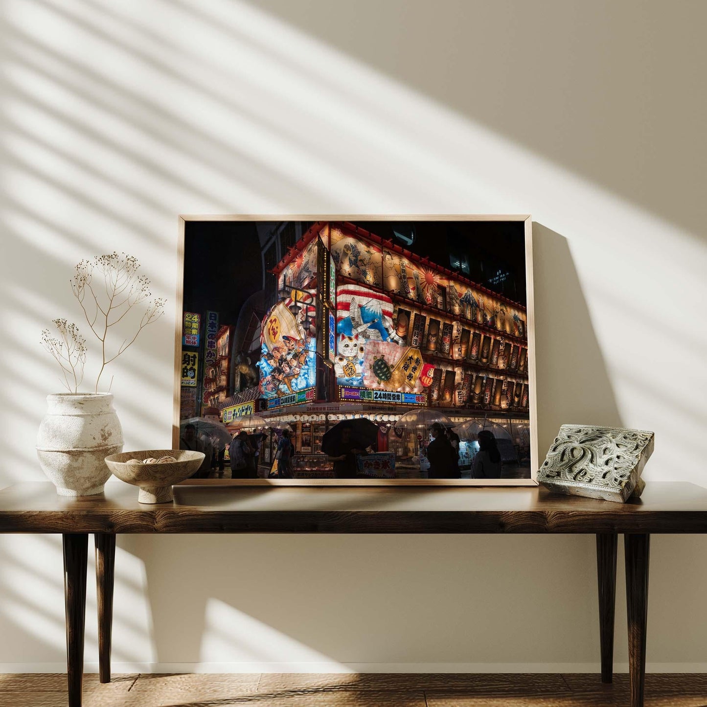The framed Shinsekai At Night cityscape photo sits on a wooden table with decorative items in a sunlit room.