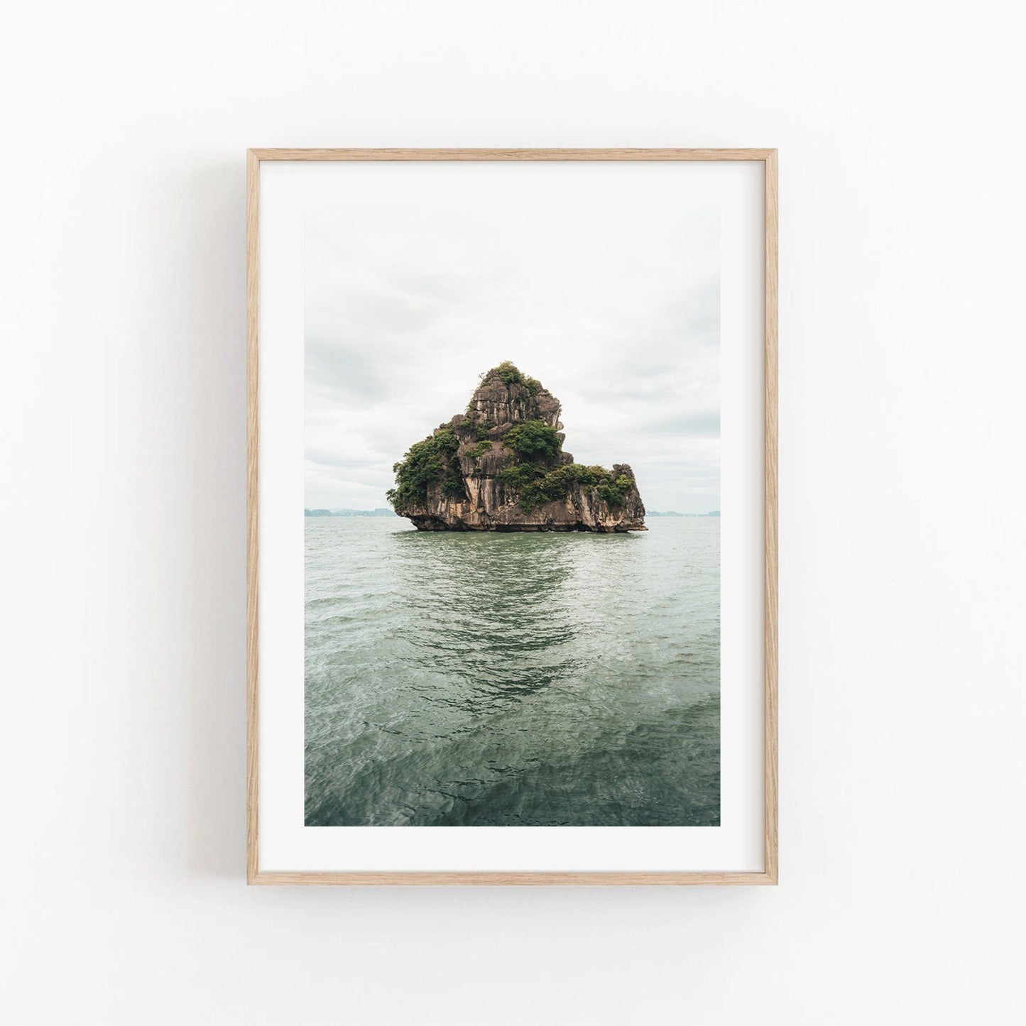 Framed photo titled Solo Limestone: features a rocky, tree-covered island in calm water, beneath a cloudy sky.