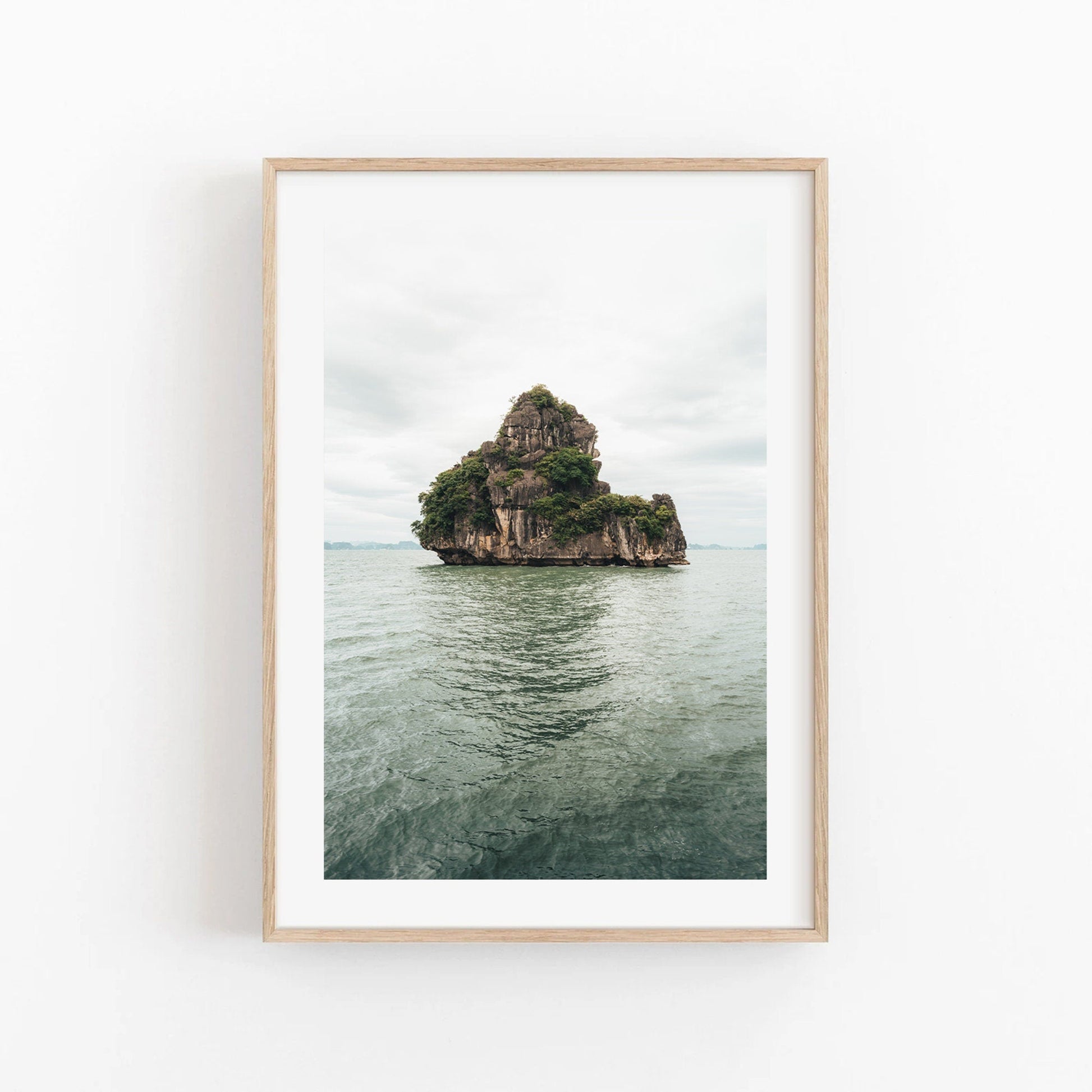 Framed photo titled Solo Limestone: features a rocky, tree-covered island in calm water, beneath a cloudy sky.