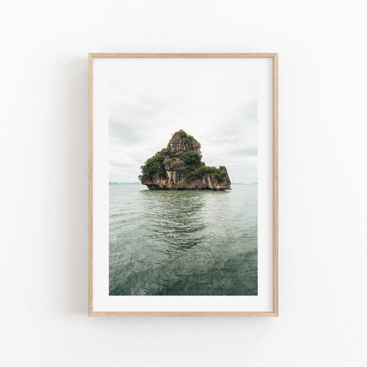 Framed photo titled Solo Limestone: features a rocky, tree-covered island in calm water, beneath a cloudy sky.