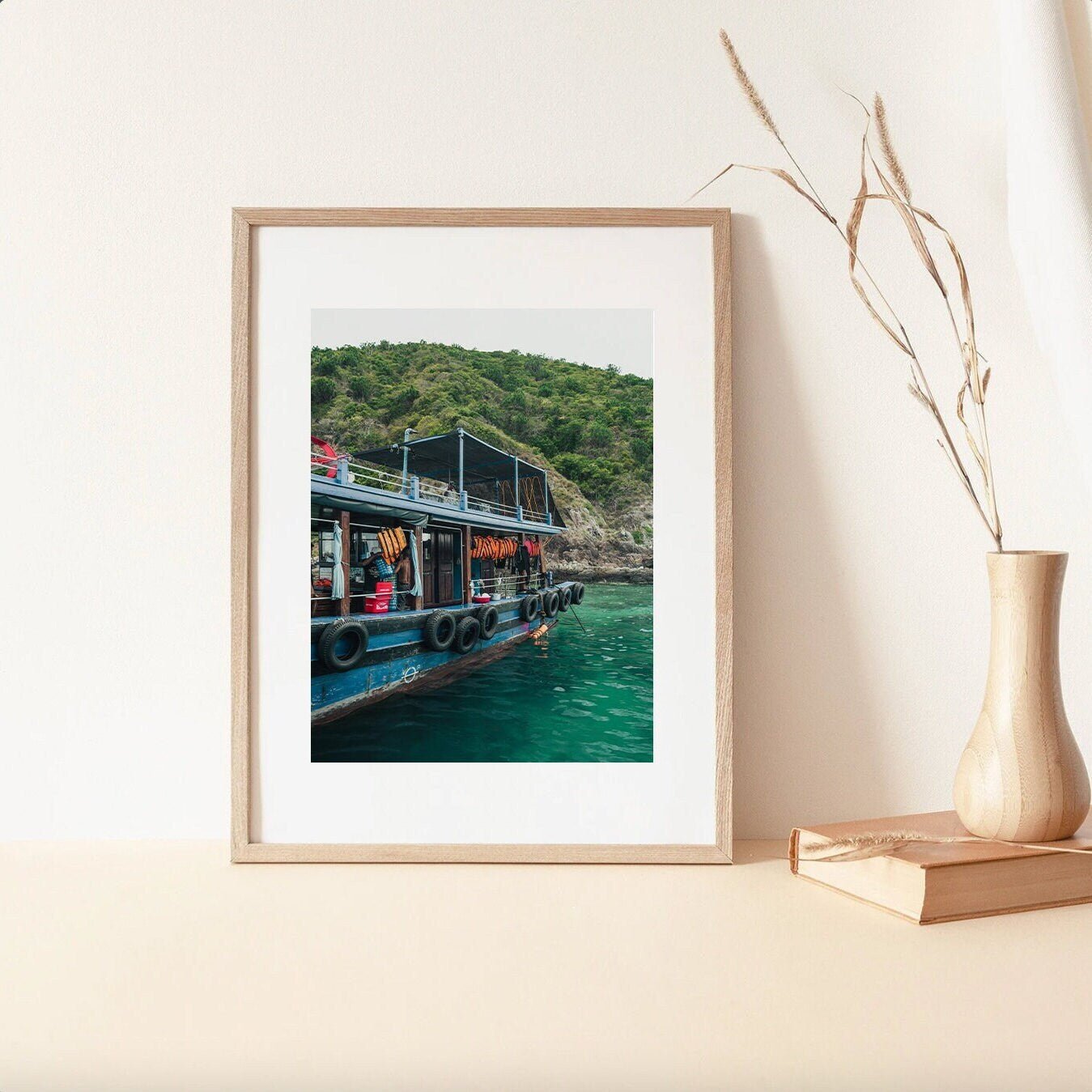 Southeast Asia Boat framed photo is displayed on a shelf with a vase and dried flowers.