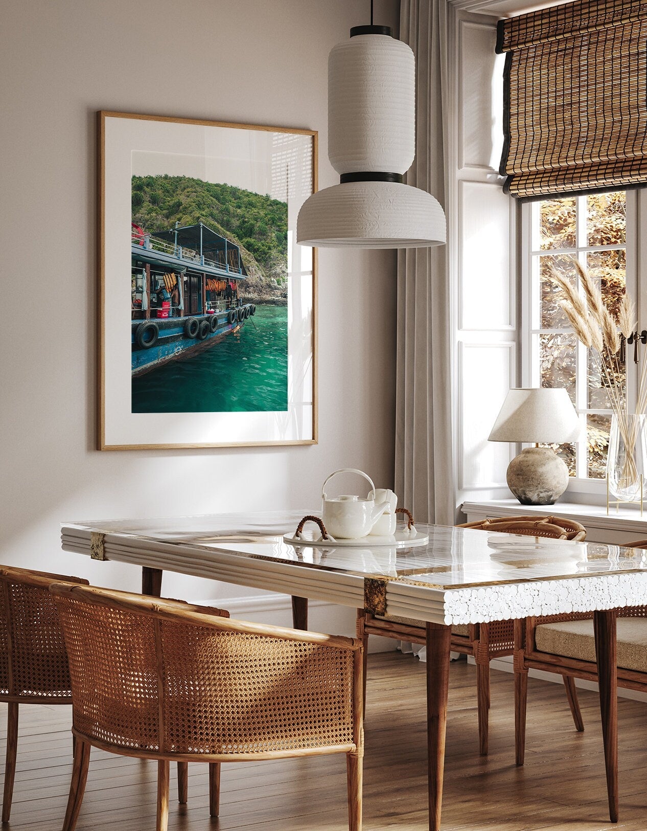 Dining area with a large framed Southeast Asia Boat photo, wicker chairs, white table, and natural sunlight.