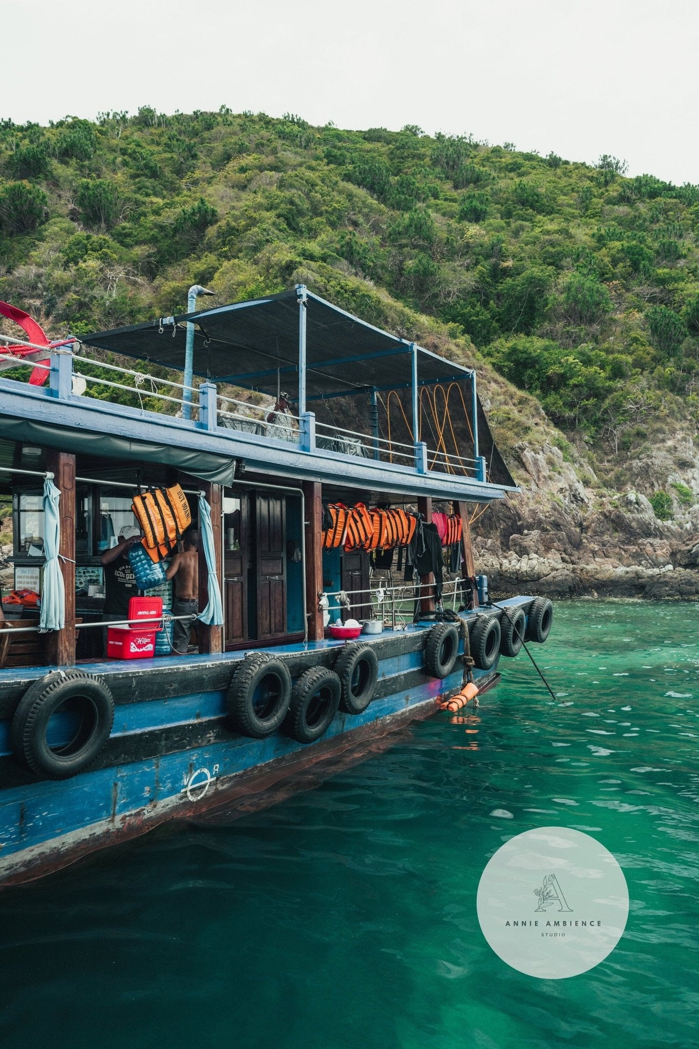 Southeast Asia Boat docked by a lush, green island with life jackets, surrounded by calm, clear turquoise water.