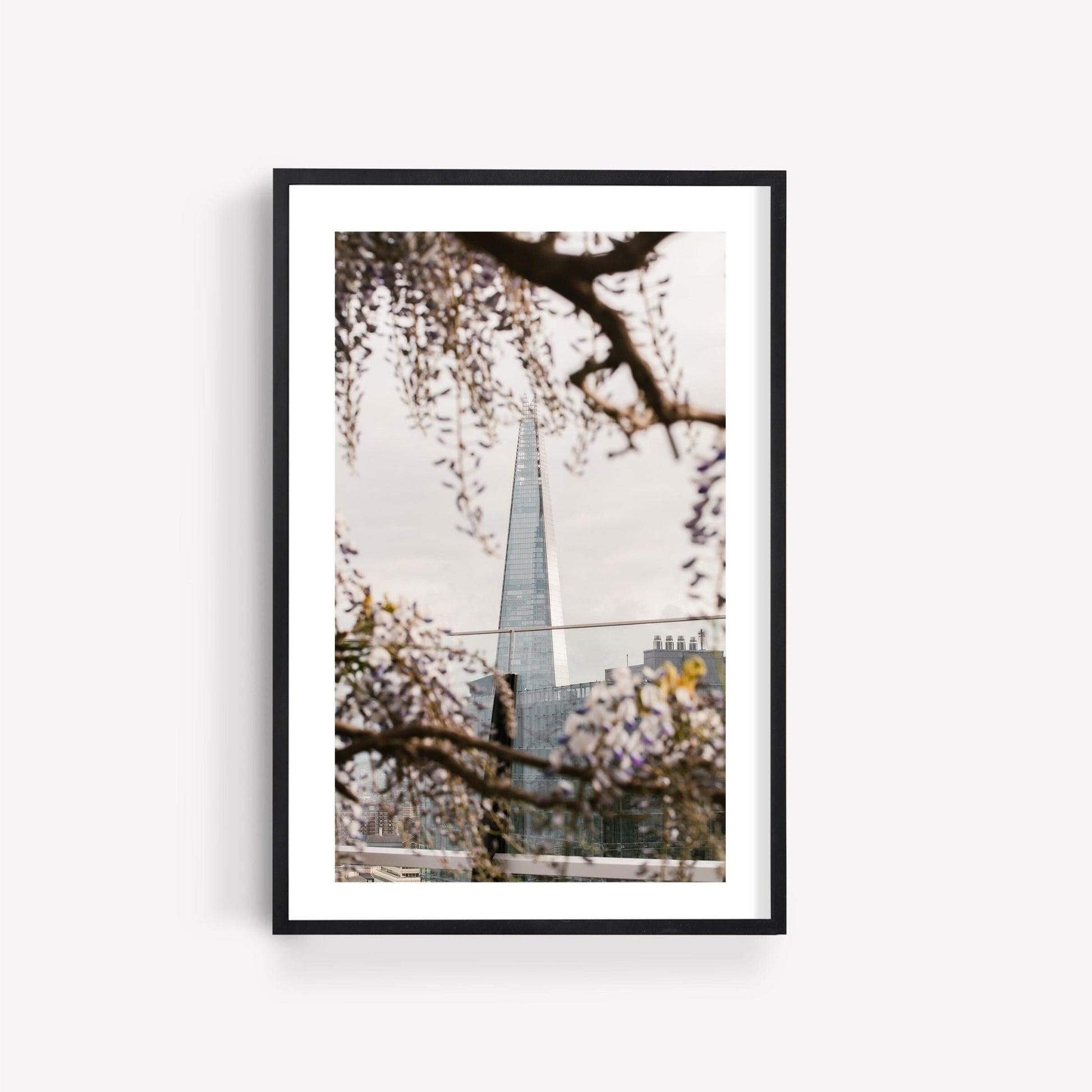 Springtime Shard: Framed photo of a modern skyscraper among flowering branches beneath a cloudy sky.