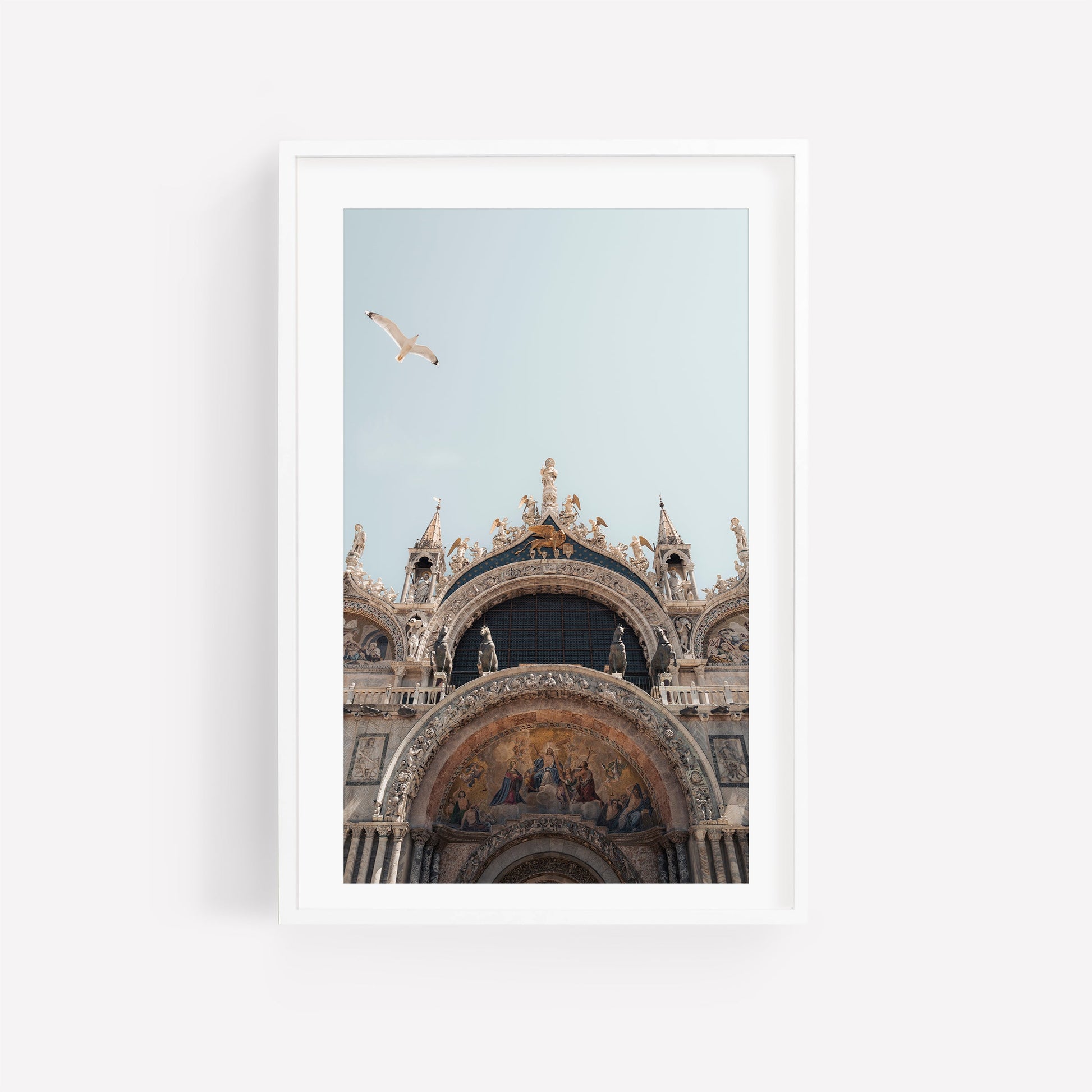 Framed photo of St. Marks Basilica facade with a seagull soaring above against a pale blue sky.