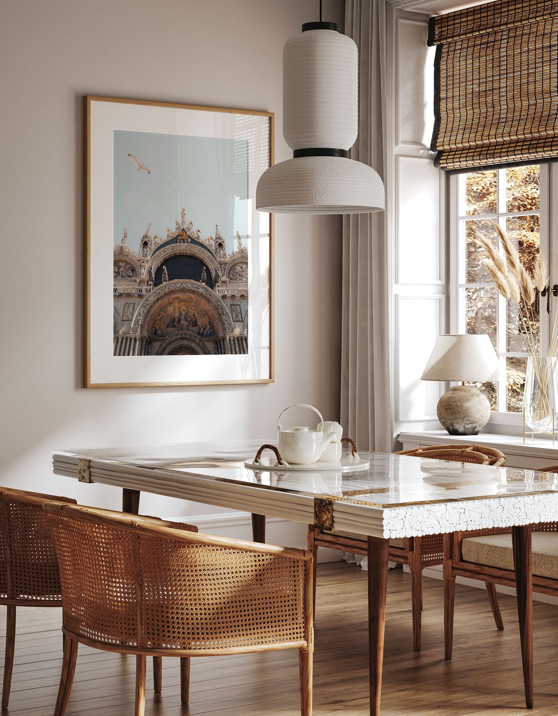 A cozy dining room with a St. Marks Basilica marble table, wicker chairs, framed art, and sunlight through bamboo blinds.