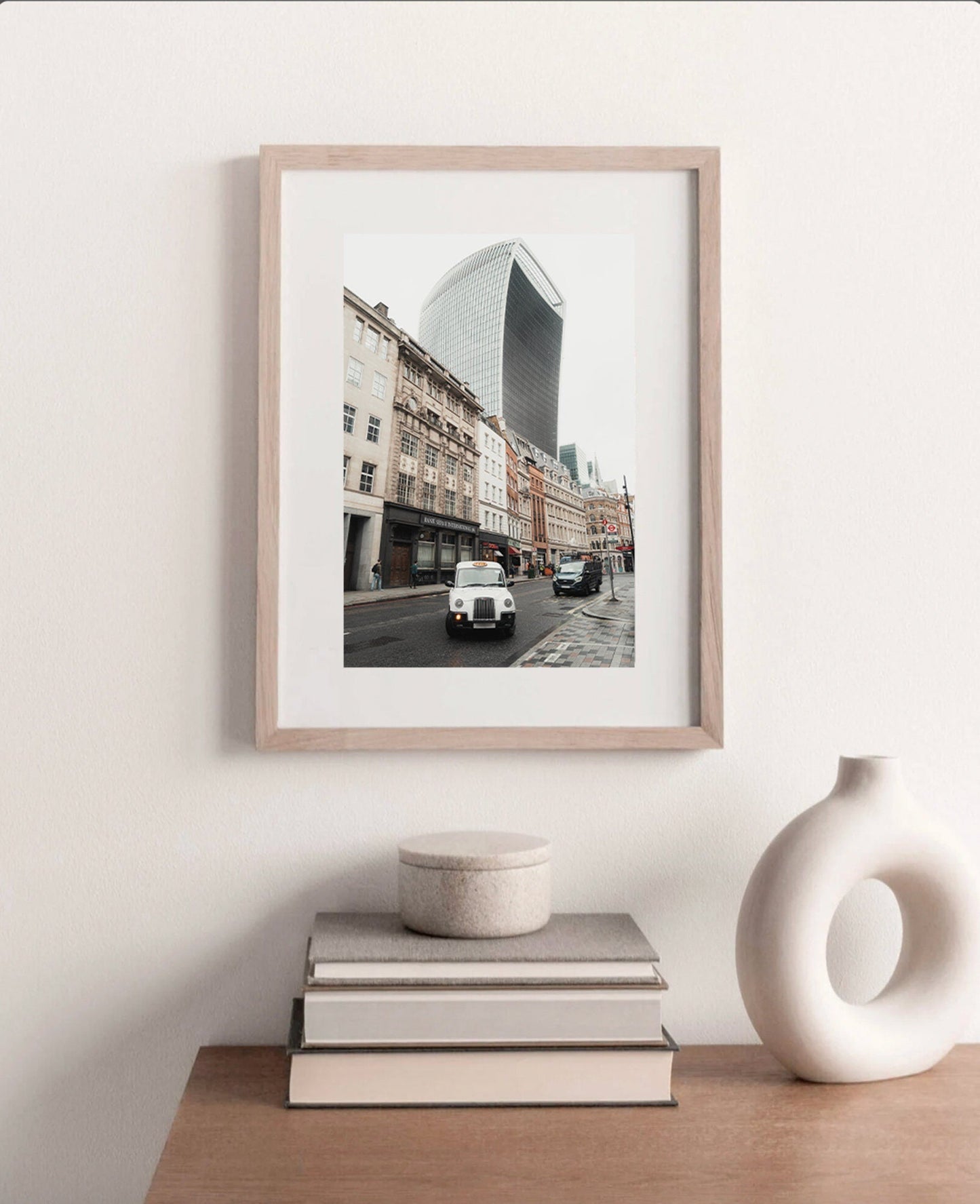 Framed Streets of London photo featuring a white car, buildings, and a skyscraper on a table with books and a vase.