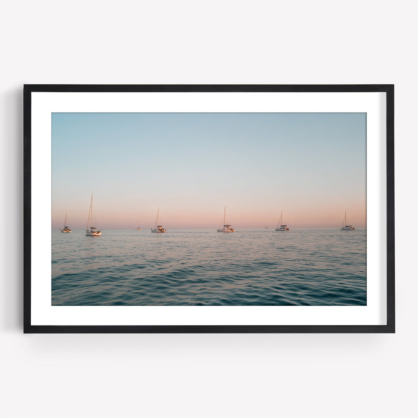 Sunset Formation framed photo features sailboats on calm ocean water at sunset beneath a pastel sky.
