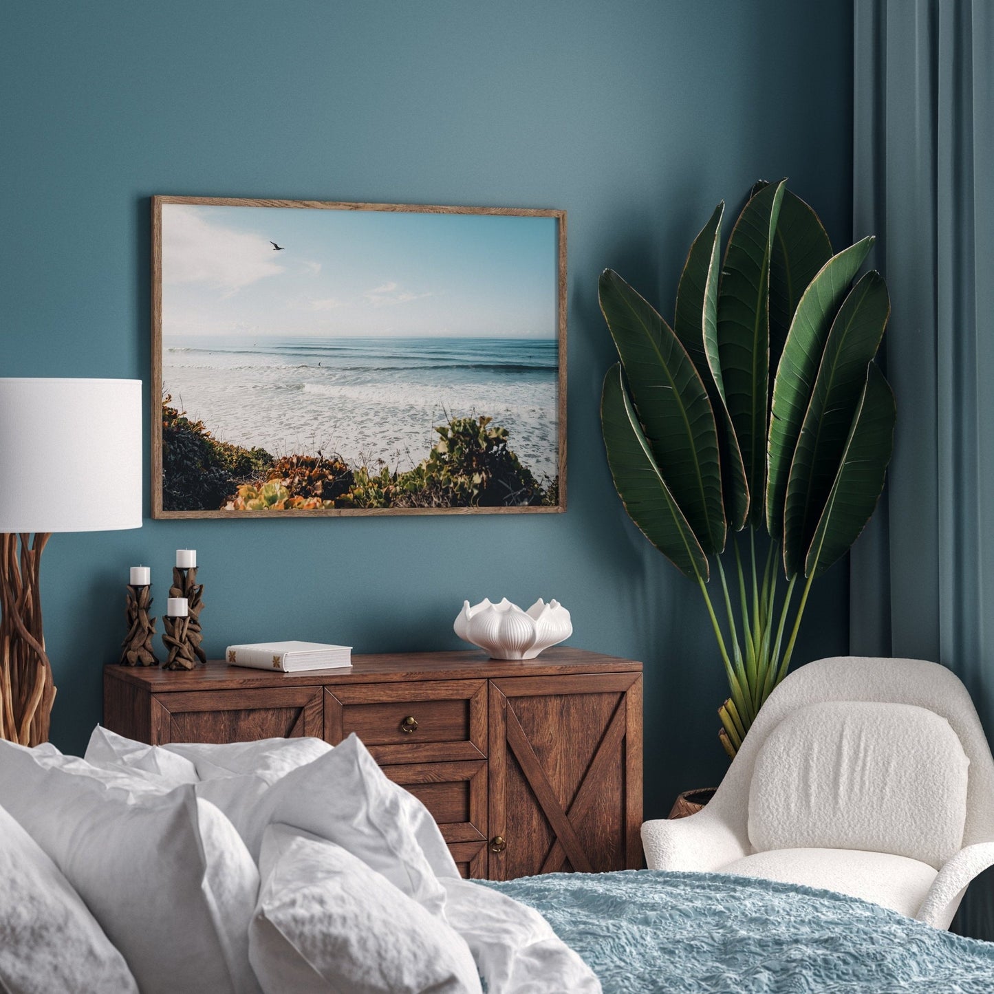 Cozy beach-themed bedroom featuring the Surf and Sky painting, a large plant, wooden furniture, and teal walls.