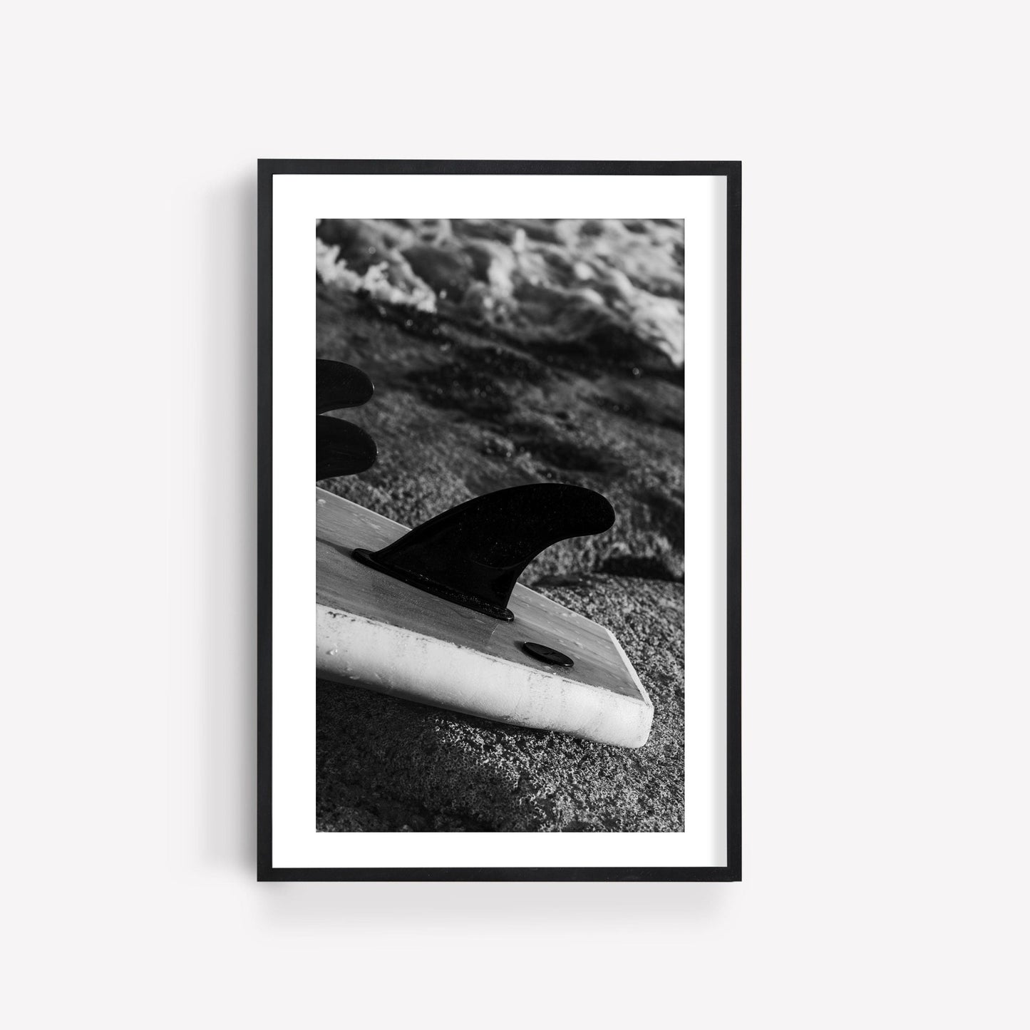 Black and white photo of the Surf Fins Black and White surfboard on a sandy beach, framed in black and white.