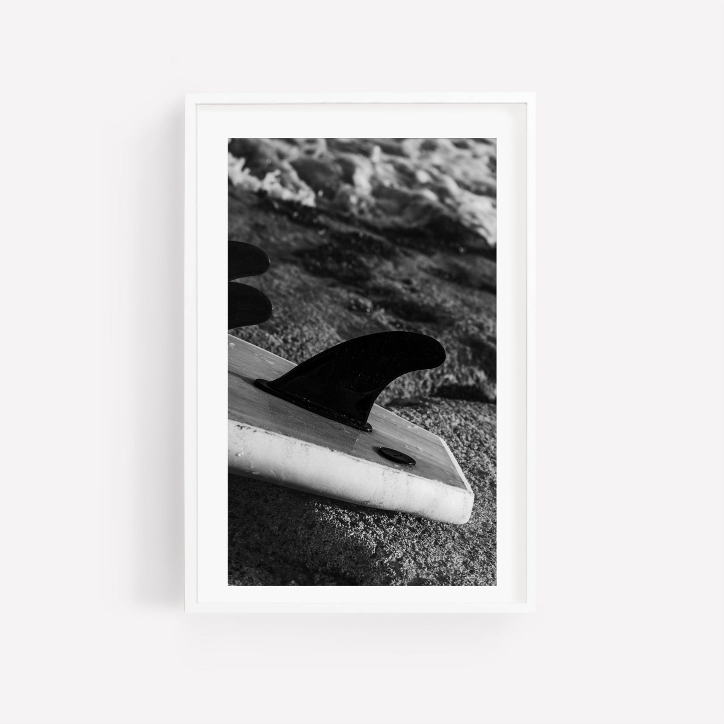 Photo of Surf Fins Black and White surfboard on sandy beach by the ocean.