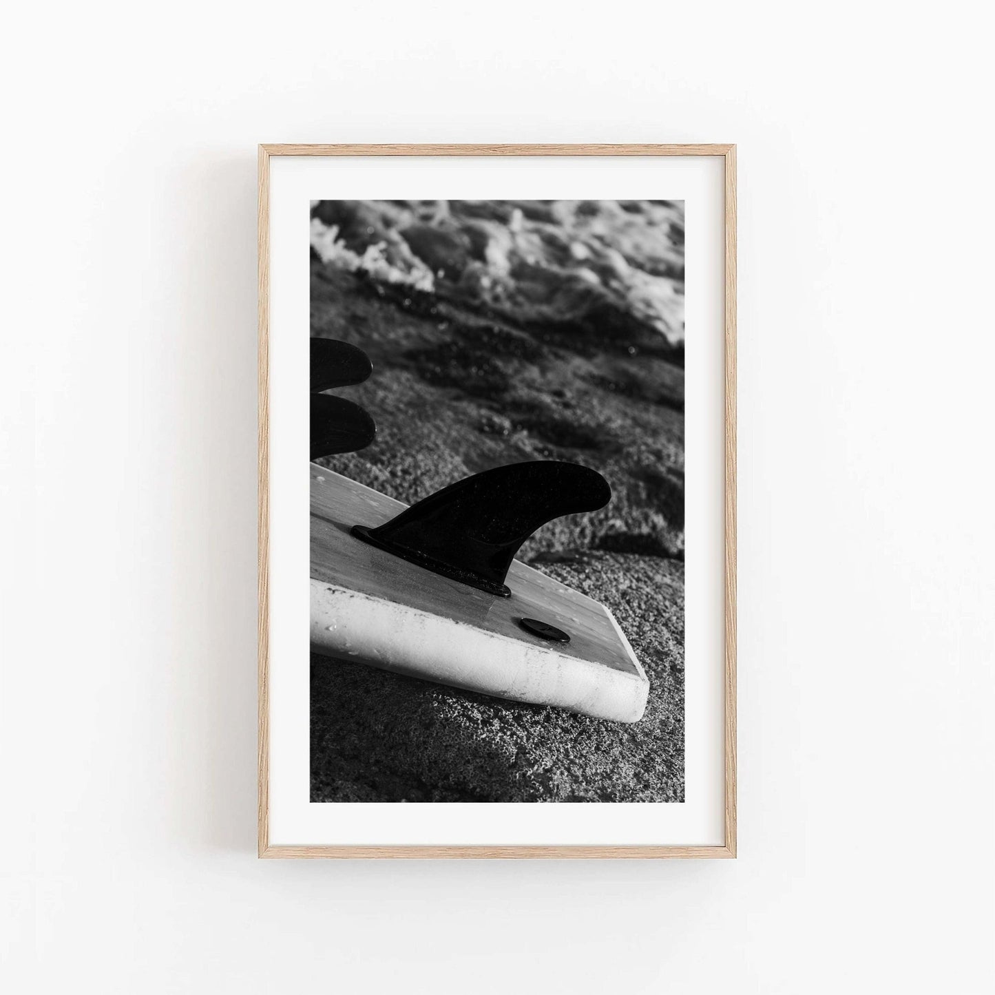 Surf Fins Black and White photo: a black & white surfboard fin on sand, waves behind, framed in light wood.