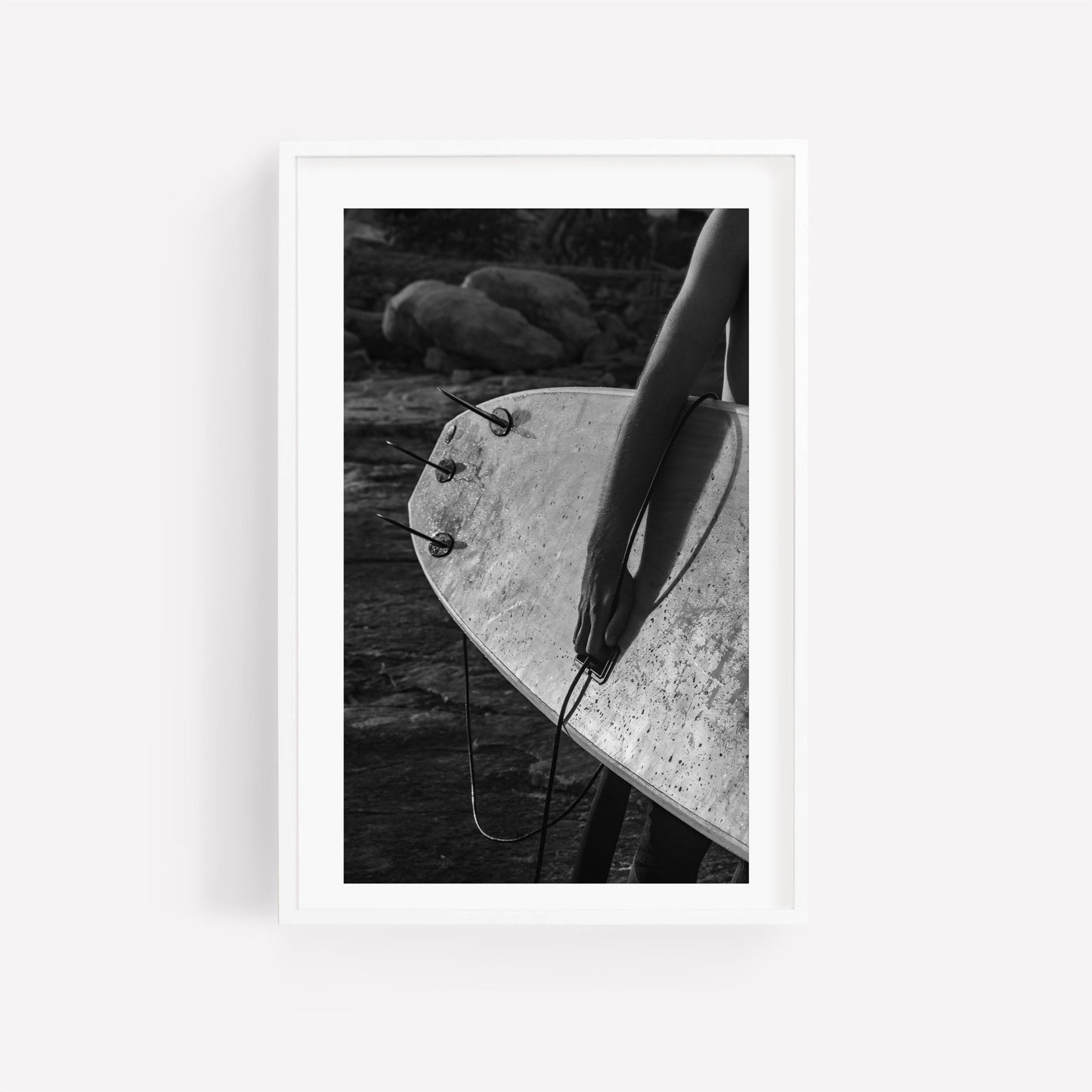 Black and white Surf Spirit photo of person with surfboard on rocky beach.