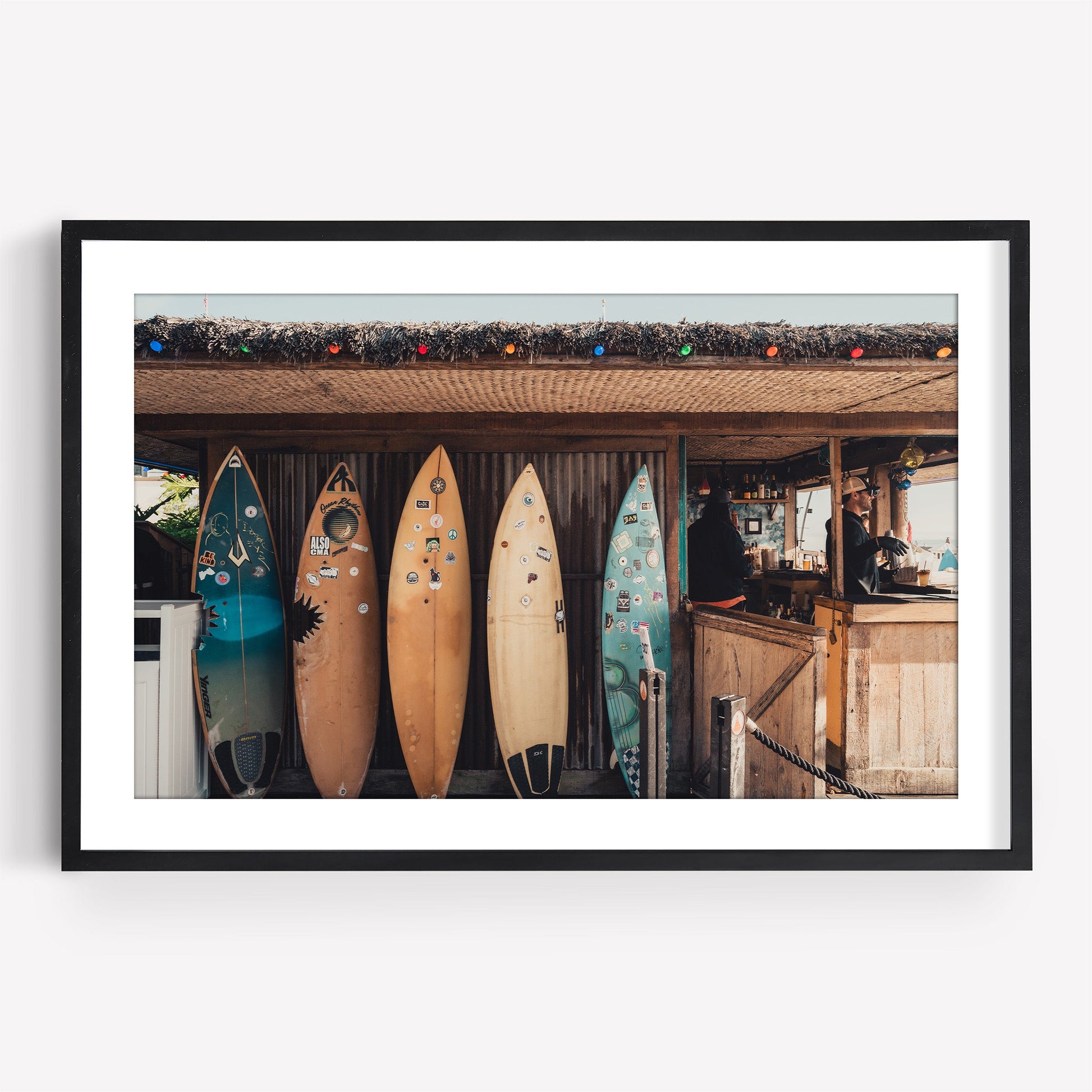 Framed photo titled Surfboard Cafe: Five upright surfboards in front of a shack with someone behind the counter inside.