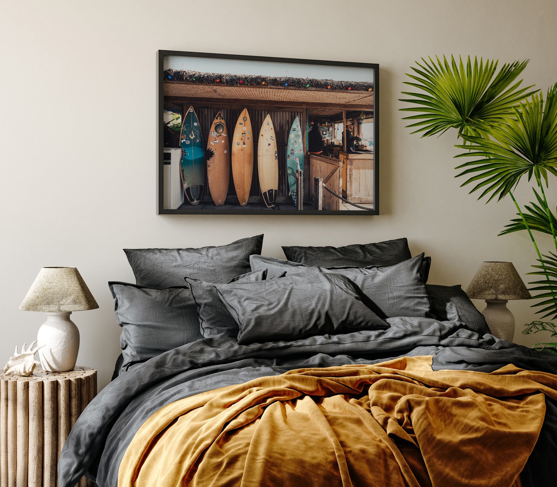 Cozy bedroom with gray and mustard bedding, a Surfboard Cafe picture above the bed, and a leafy plant bedside.