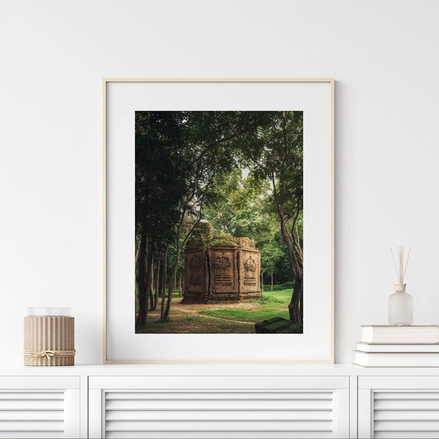 Framed Temple I photo on modern white shelf with decor items, small brick structure amid trees.
