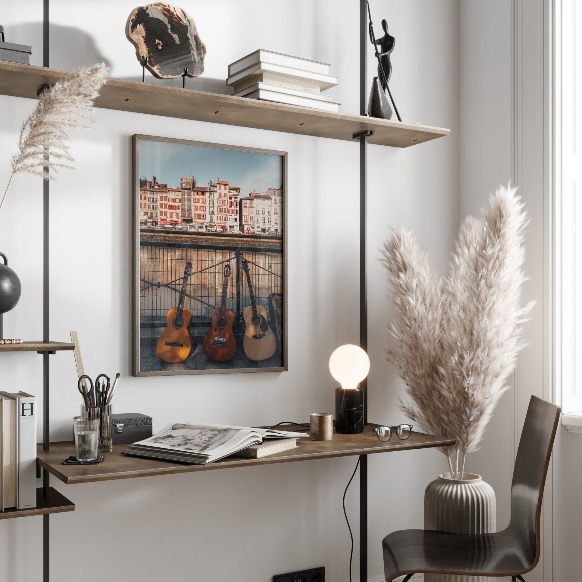 Minimalist workspace with wooden desk, guitar art titled Three Guitars, lamp, pampas grass, and floating shelves for books and decor.