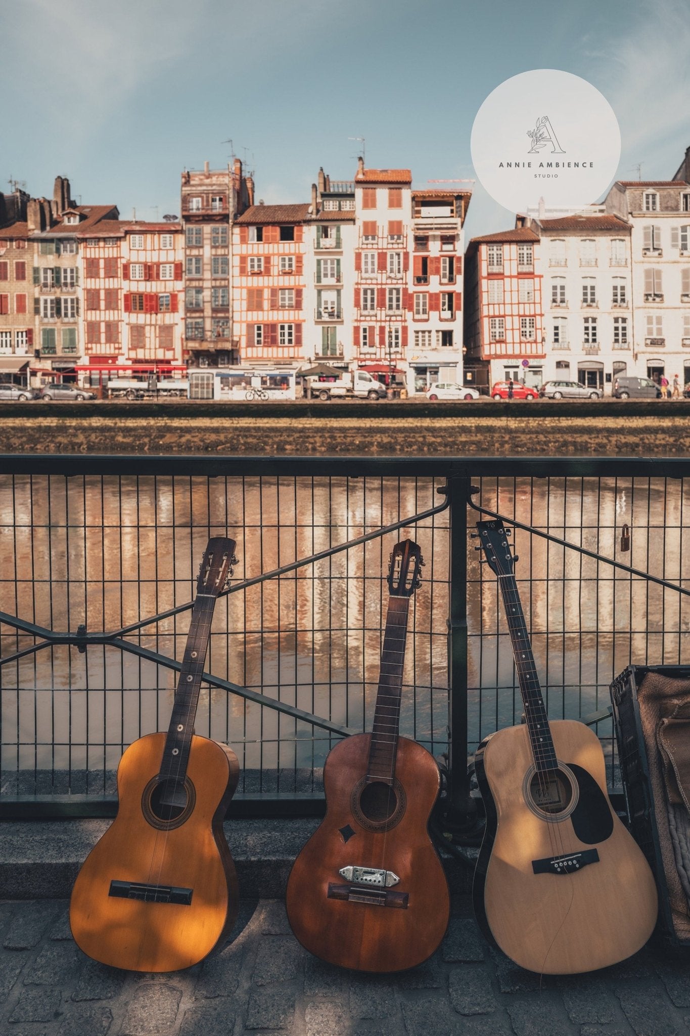Product Three Guitars features guitars against a riverside fence with colorful buildings and a clear sky backdrop.