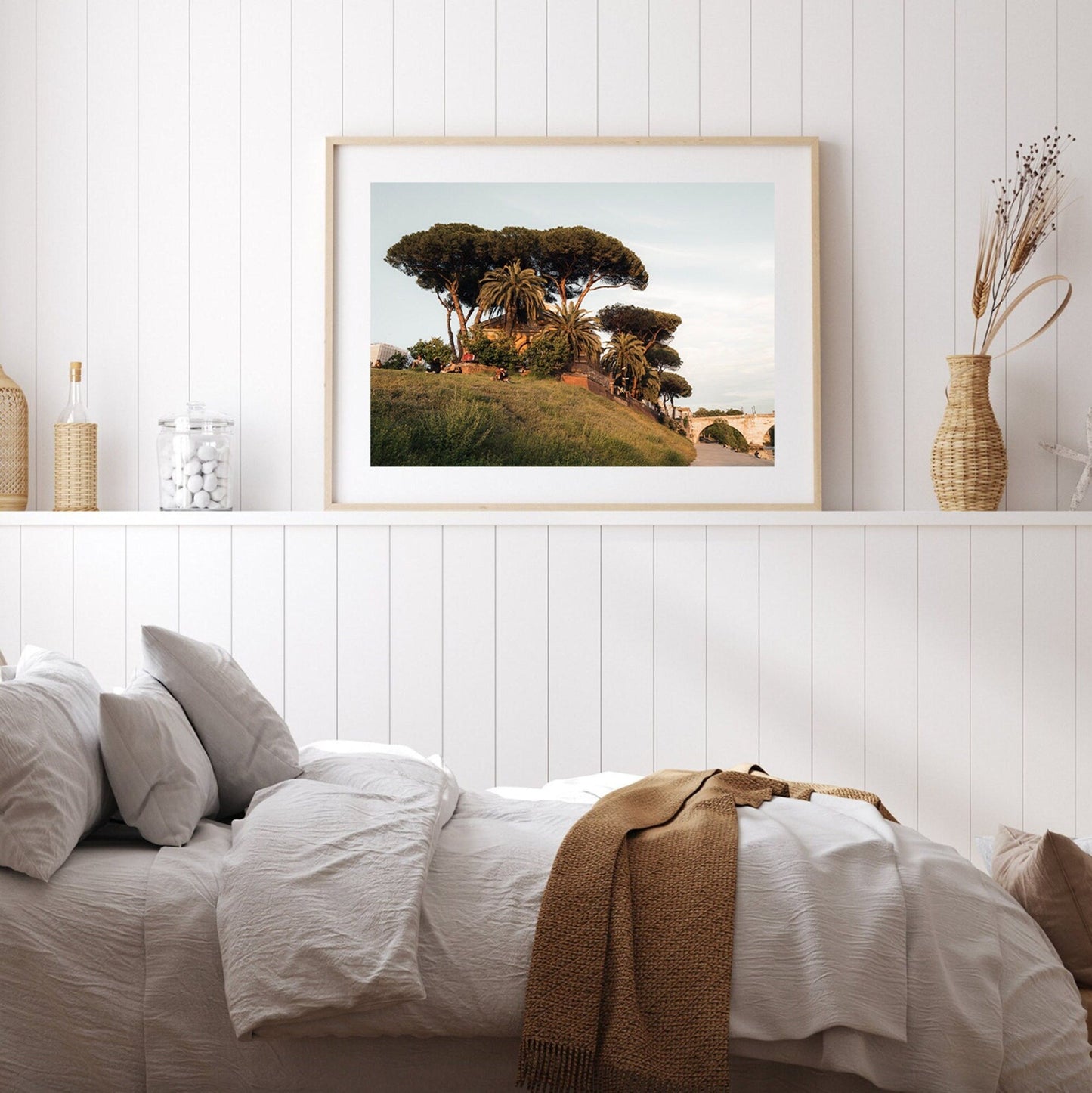 A cozy bedroom with Tiber Island Delight I above the bed, green trees, and a golden brown blanket draped over.