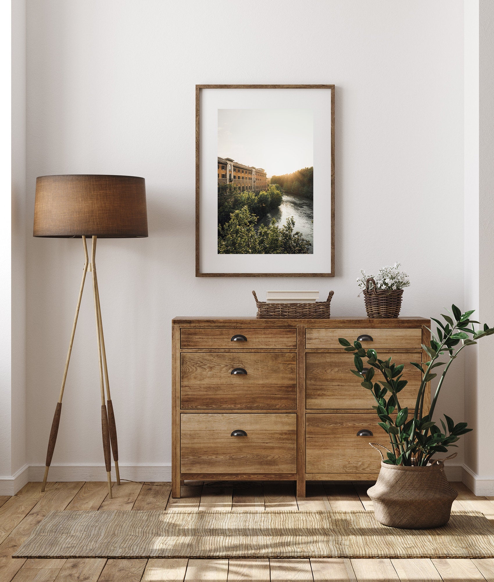 A cozy room with Tiber Island Glow decor: wooden dresser, potted plant, tall lamp, and landscape artwork on the wall.