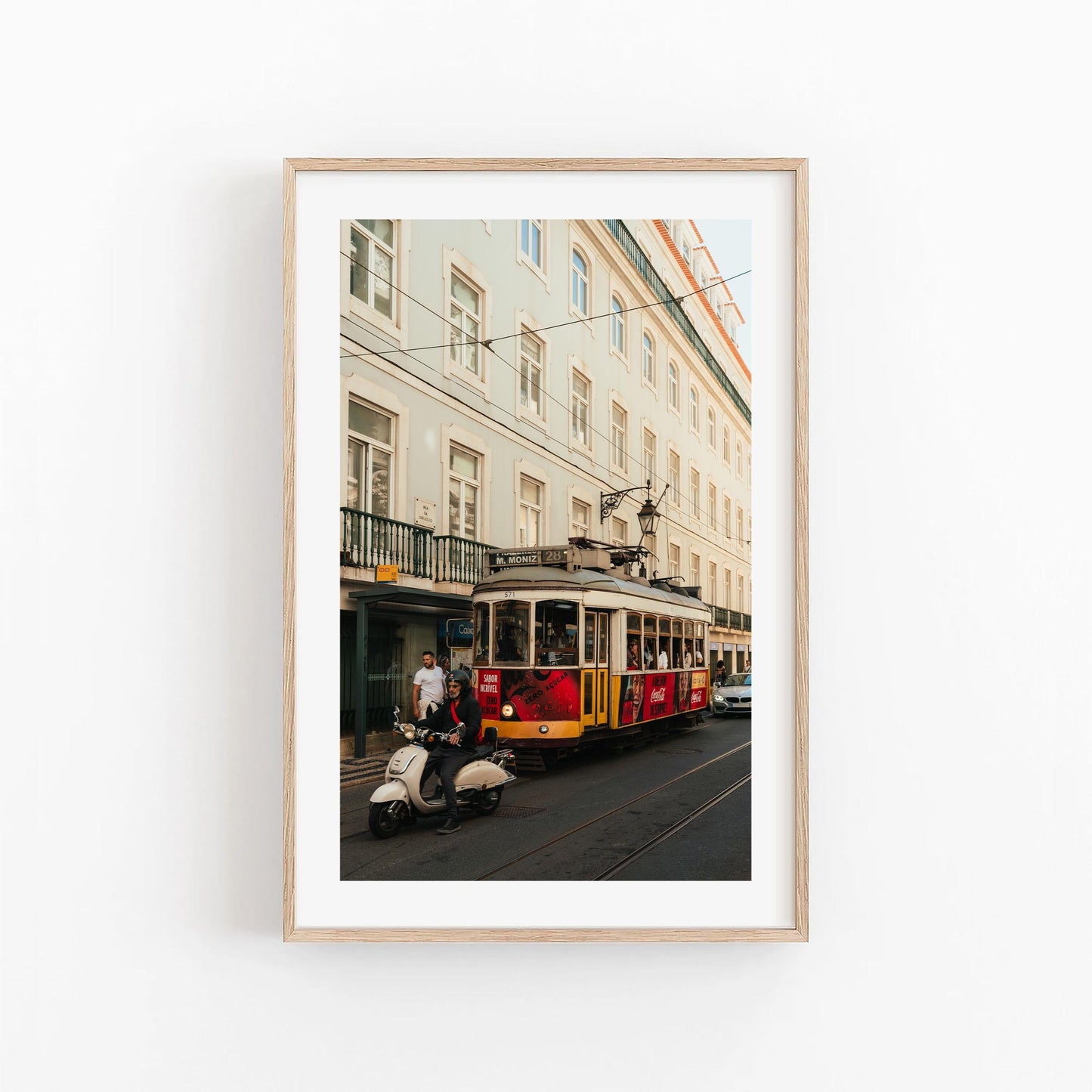 Framed photo titled "Tram 28" shows a person on a scooter passing a red and yellow tram by a light building.
