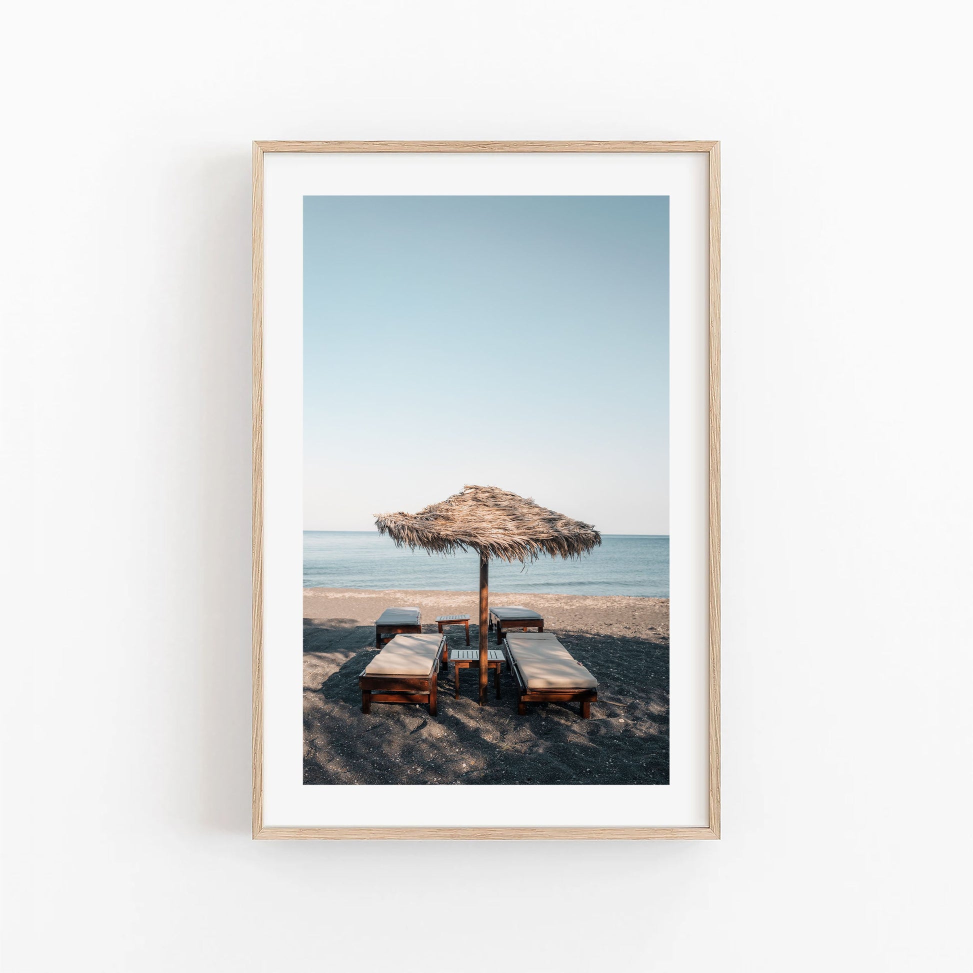 Tranquil Shade: Framed photo of lounge chairs under a thatched umbrella facing the calm sea.