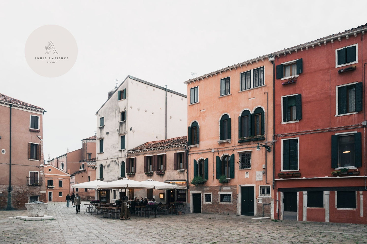 Venice Piazza features outdoor seating in a quiet square, surrounded by rustic buildings beneath a cloudy sky.