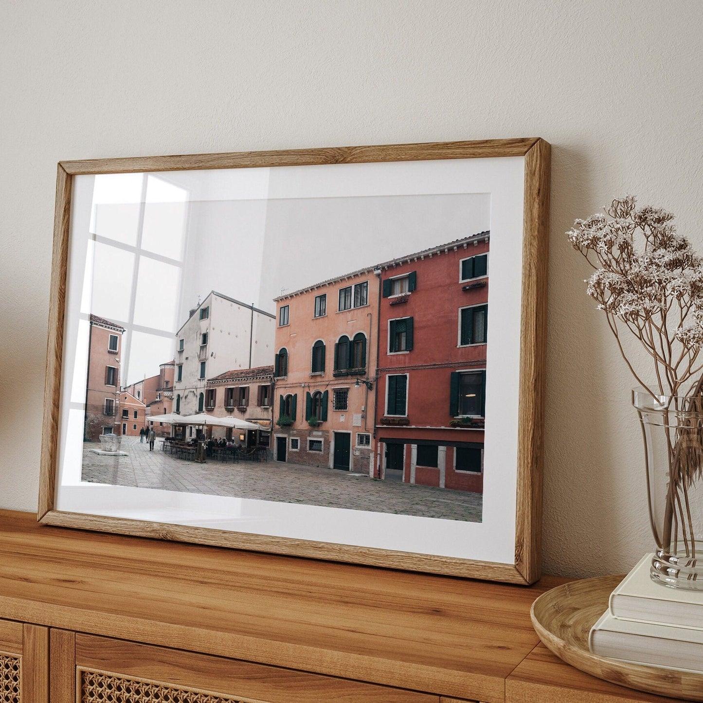 Venice Piazza framed photo of colorful buildings on a wooden sideboard with dried flowers in a vase.
