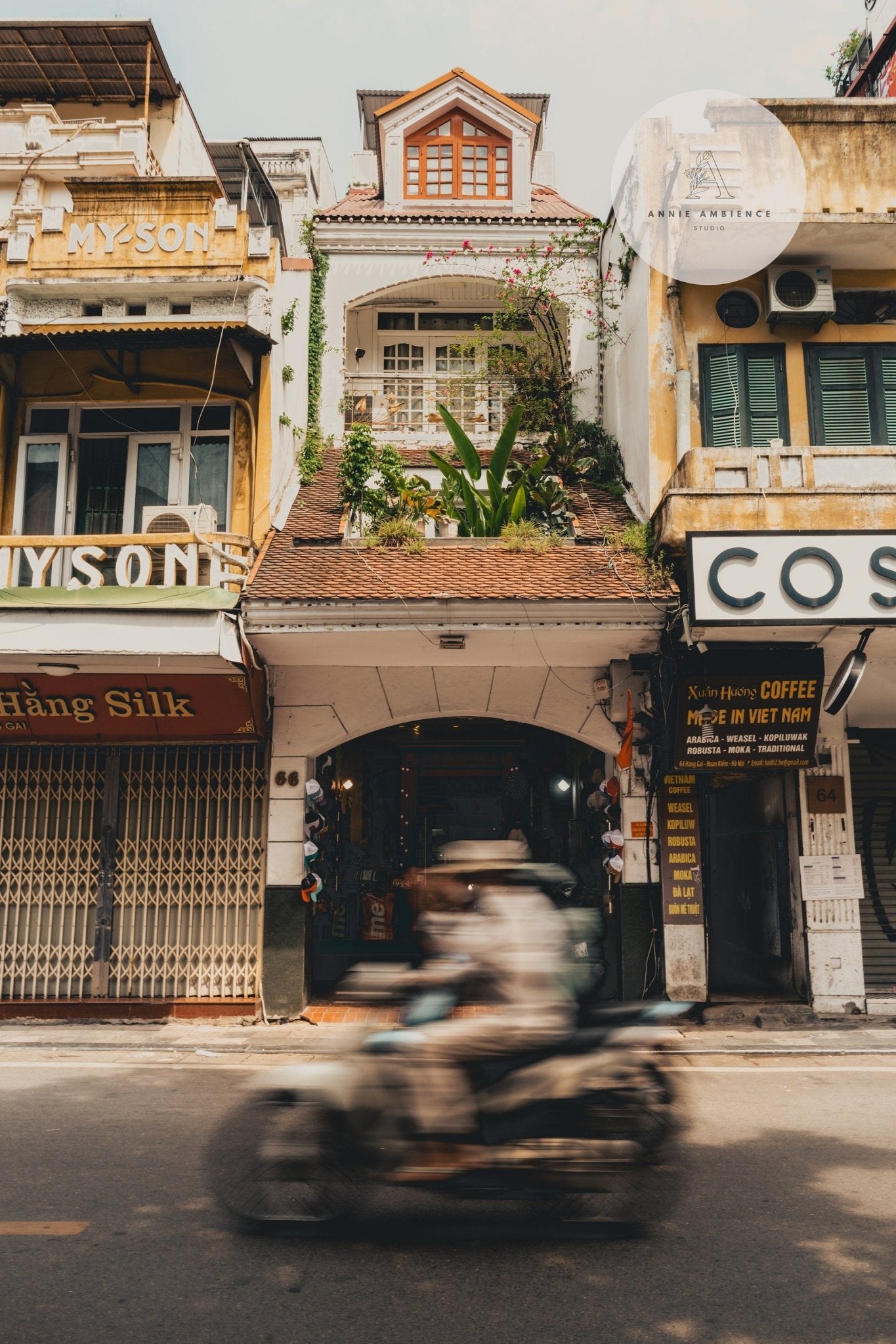 A motorbike rider weaves past old shops and narrow buildings on a busy Hanoi street in Pace of Hanoi.
