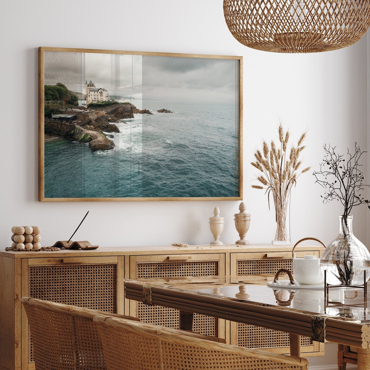 The Villa Beltza photo hangs in a dining room with wicker furniture, decorative jars, and a glass vase on the table.