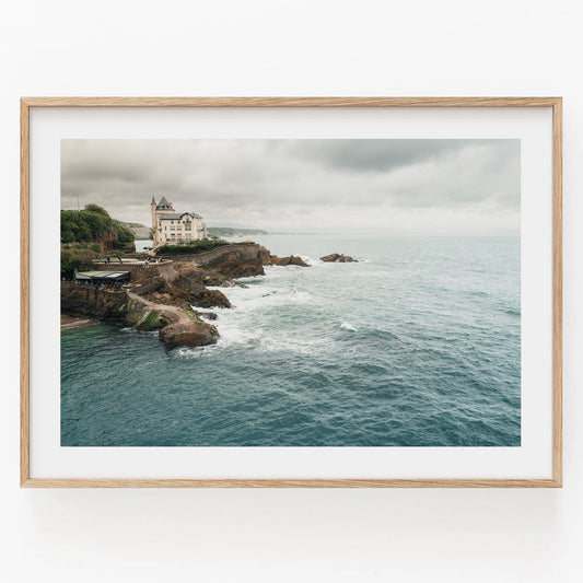 Framed photo of Villa Beltza, a coastal cliff house overlooking the ocean under a cloudy sky.