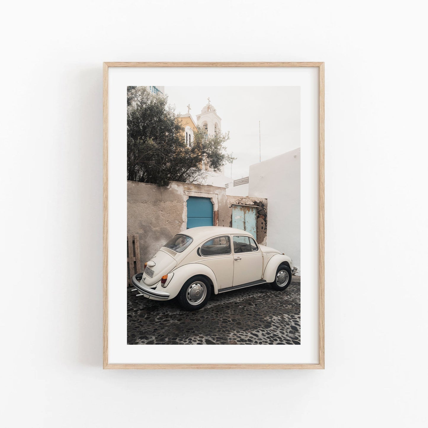 Framed photo of a vintage Volkswagen Beetle on a cobblestone street with white buildings and a blue door.