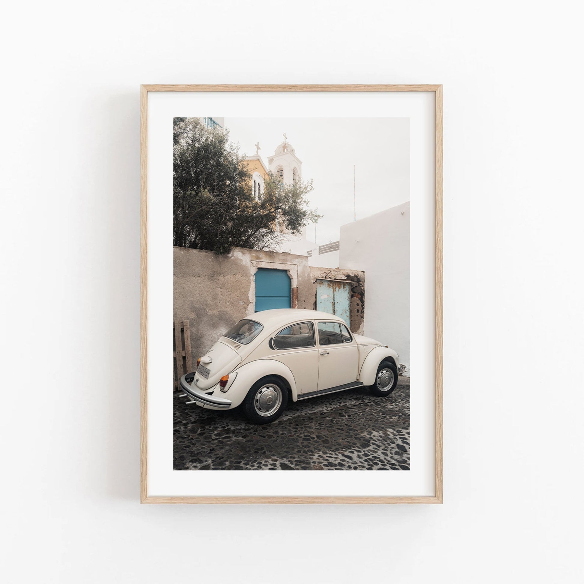 Framed photo of a vintage Volkswagen Beetle on a cobblestone street with white buildings and a blue door.