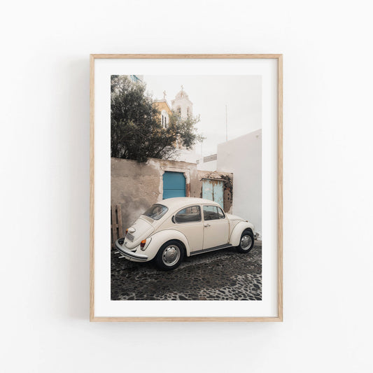 Framed photo of a vintage Volkswagen Beetle on a cobblestone street with white buildings and a blue door.
