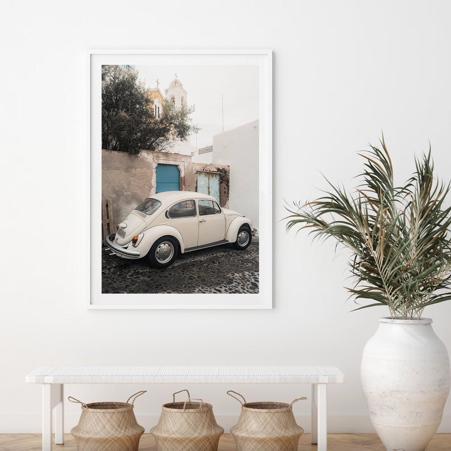 Framed photo of a Volkswagen Beetle on a cobblestone street with a bench, baskets, and potted plant in the foreground.