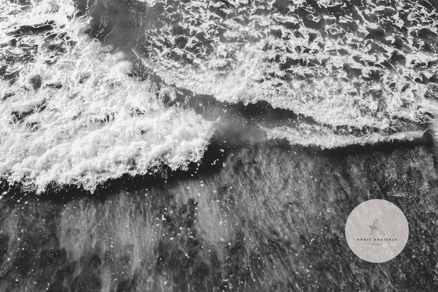 The Wave Rush Black and White captures an aerial view of ocean waves crashing onto the shore, forming a dynamic foam pattern.