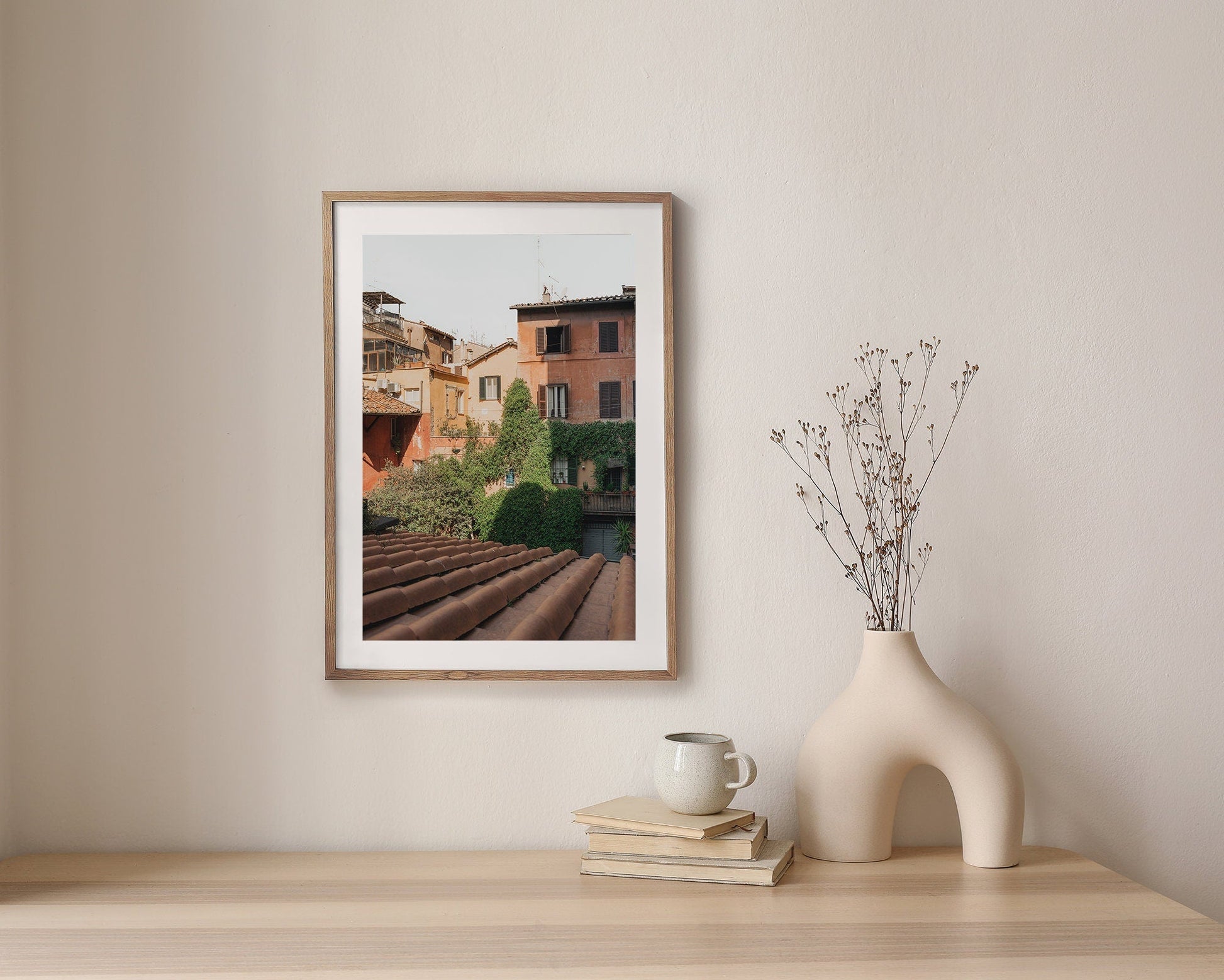 Woke Up in Rome photo on a wall, with a white vase and books on a wooden table.