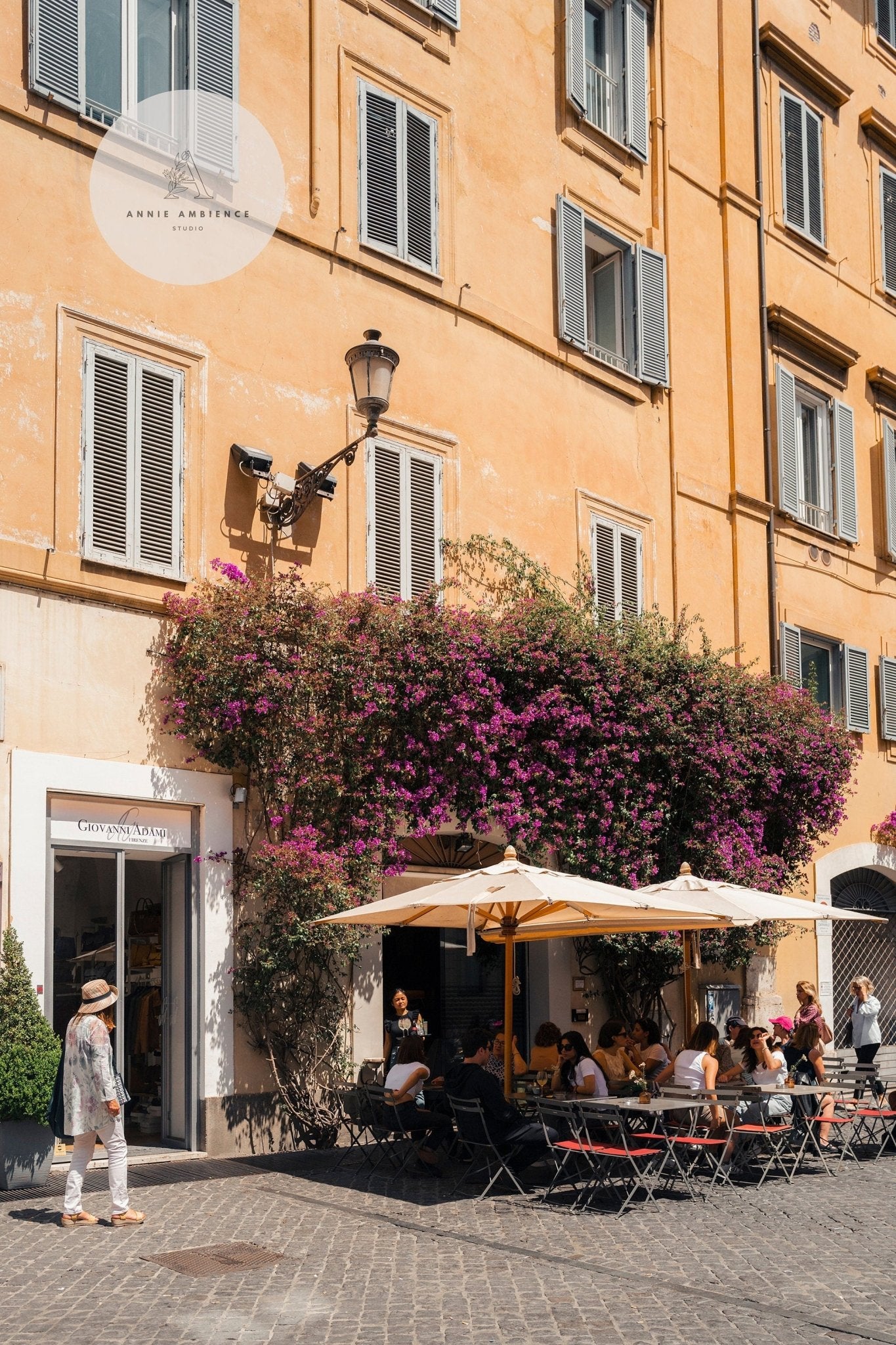 People enjoying Yellow Charm umbrellas at outdoor tables by a flower-covered building.