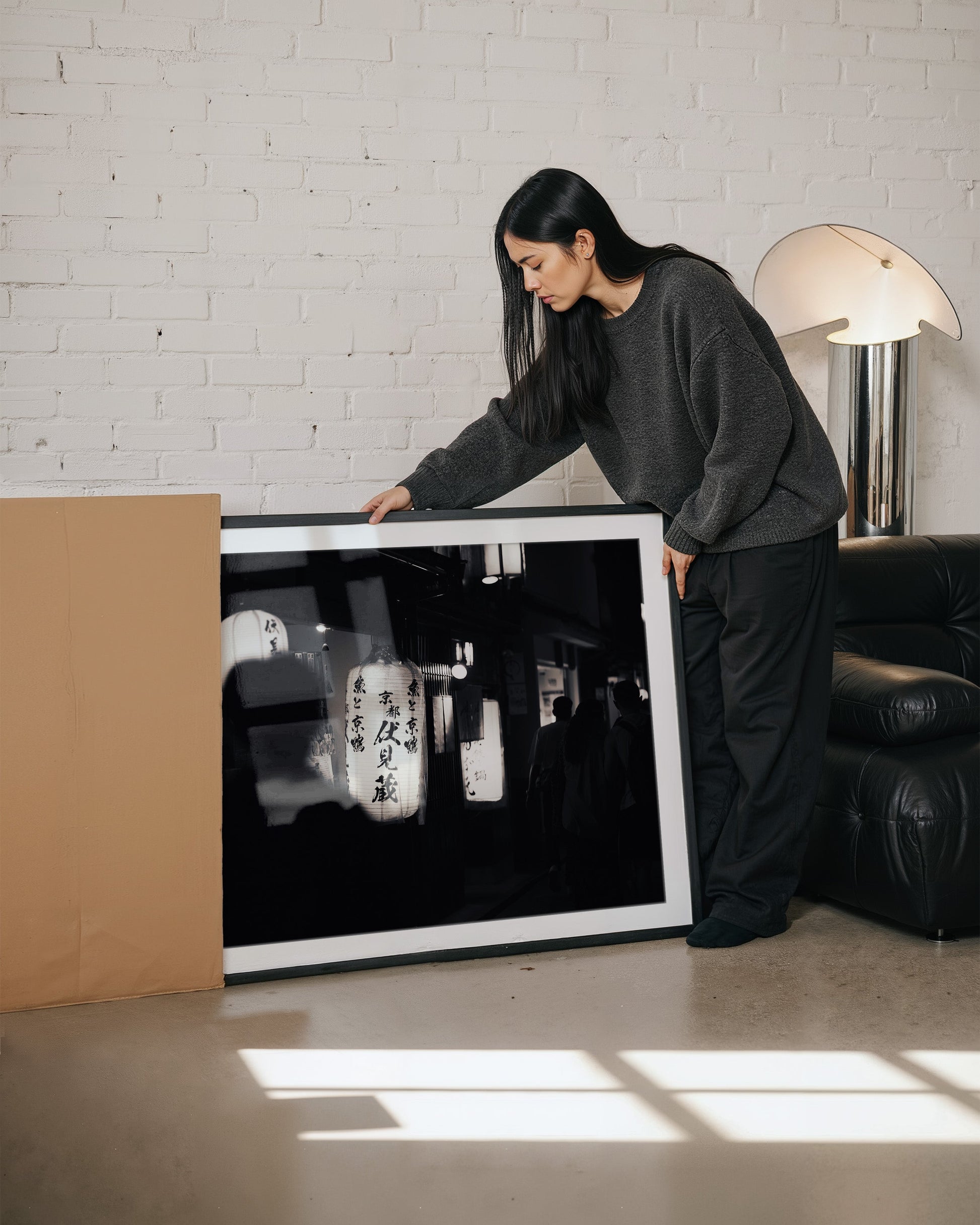 A woman unboxes and examines the large framed "Kyoto At Night Black and White" photograph in her living room.