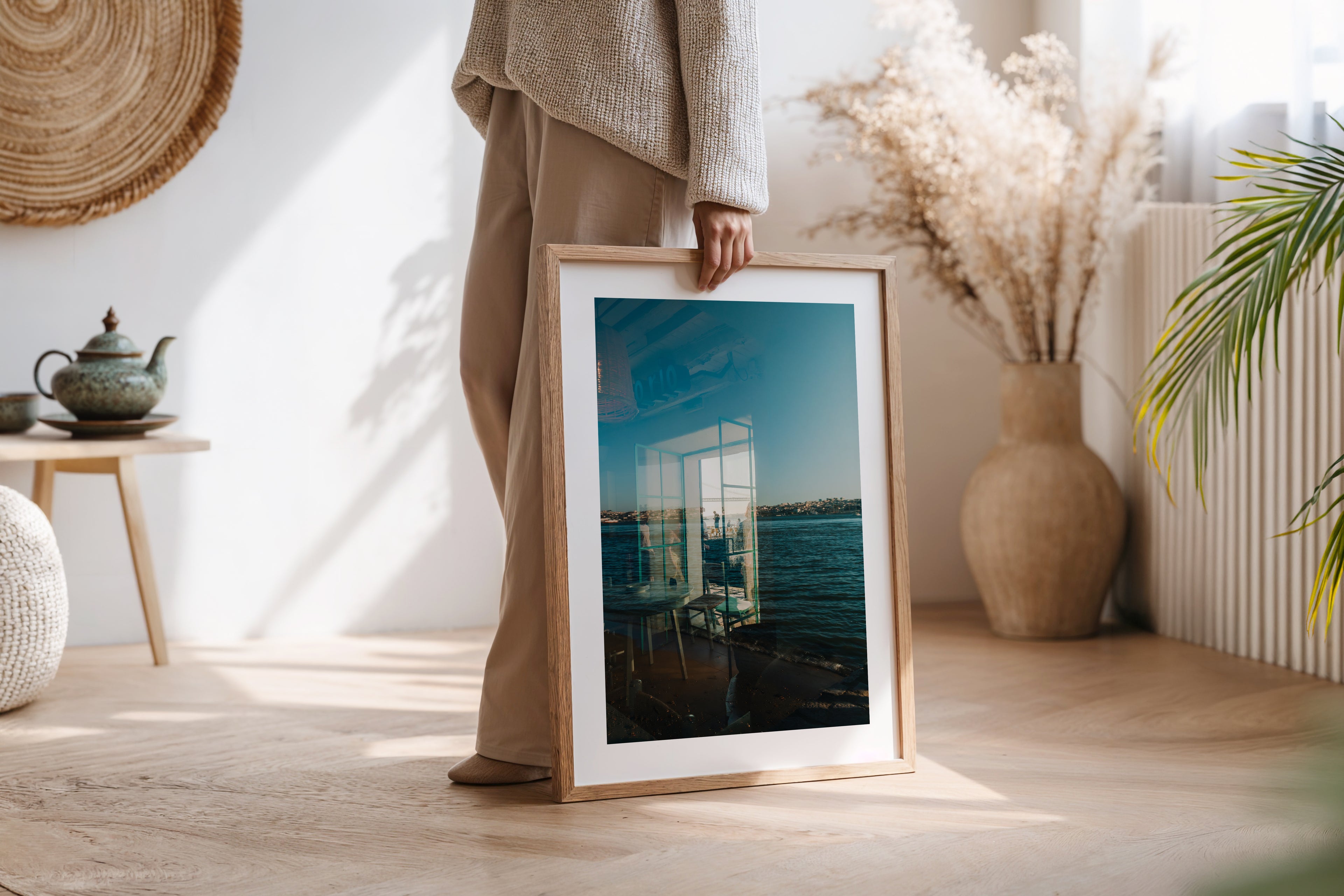 Person holding “Almada Reflections” framed photo in a bright room with plants and natural decor.