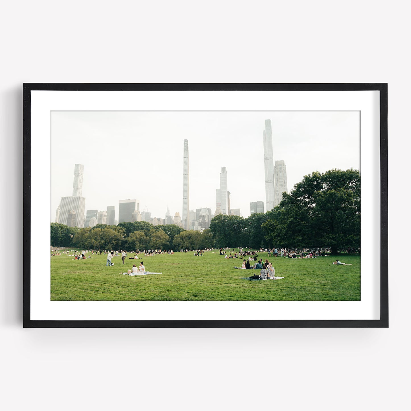 People relaxing on the Great Lawn, a grassy field in a city park with skyscrapers and trees in the background.