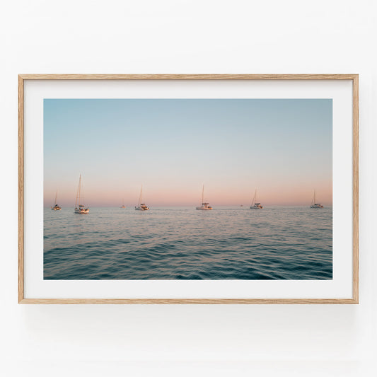 Sunset Formation—a framed photo featuring sailboats on tranquil ocean water beneath a pastel sunset sky.